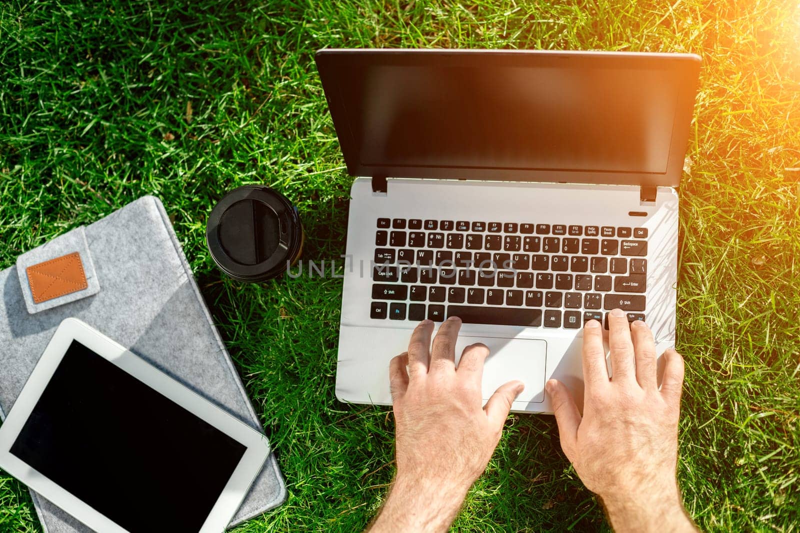 Close-up shot of handsome man's hands touching laptop computer's screen. Businessman using a laptop computer and sitting on the ground. Sun flare