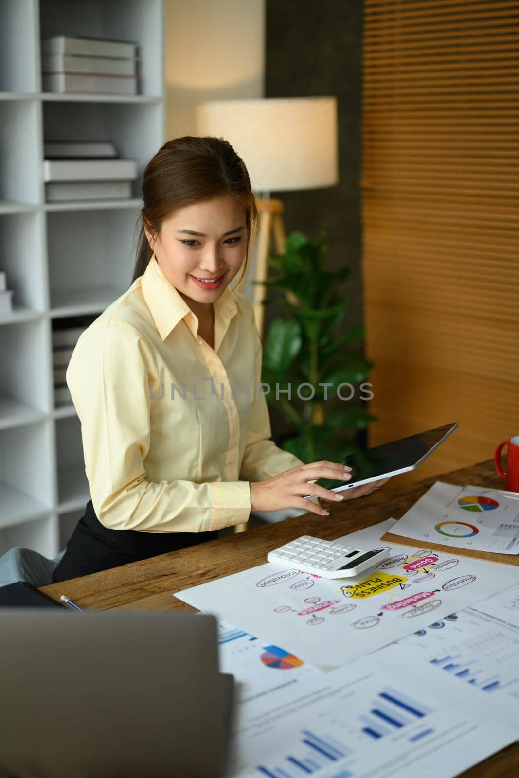 Professional female accountant sitting at office desk using digital tablet and preparing annual financial reports.