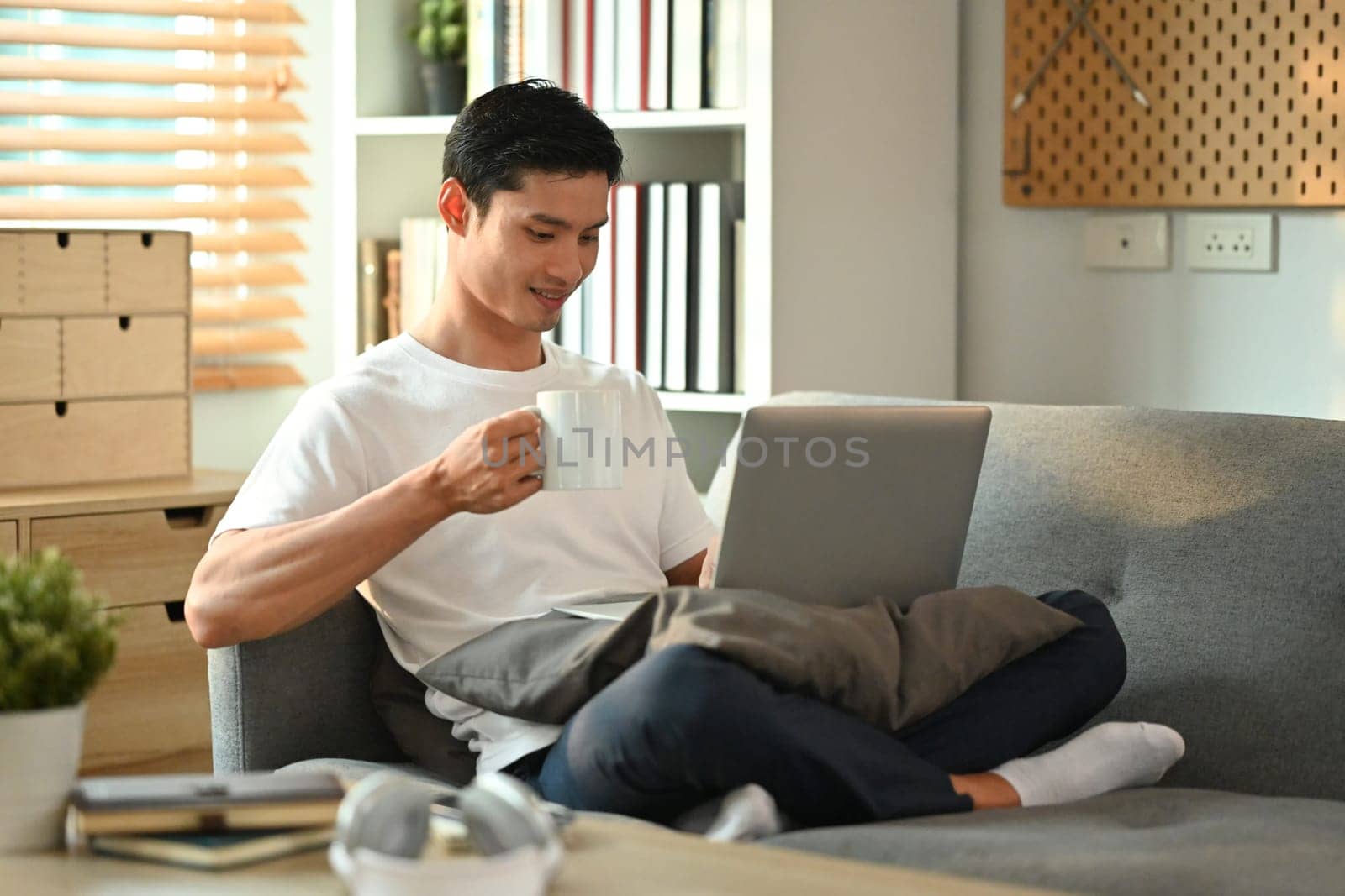 Carefree asian man drinking coffee and browsing internet, checking email on laptop. People, technology and lifestyle.