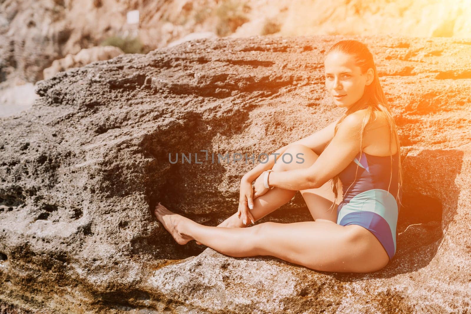 happy tourist in blue swimwear takes a photo outdoors to capture memories. The photo depicts a woman traveling and enjoying her surroundings on the beach, with volcanic mountains in the background