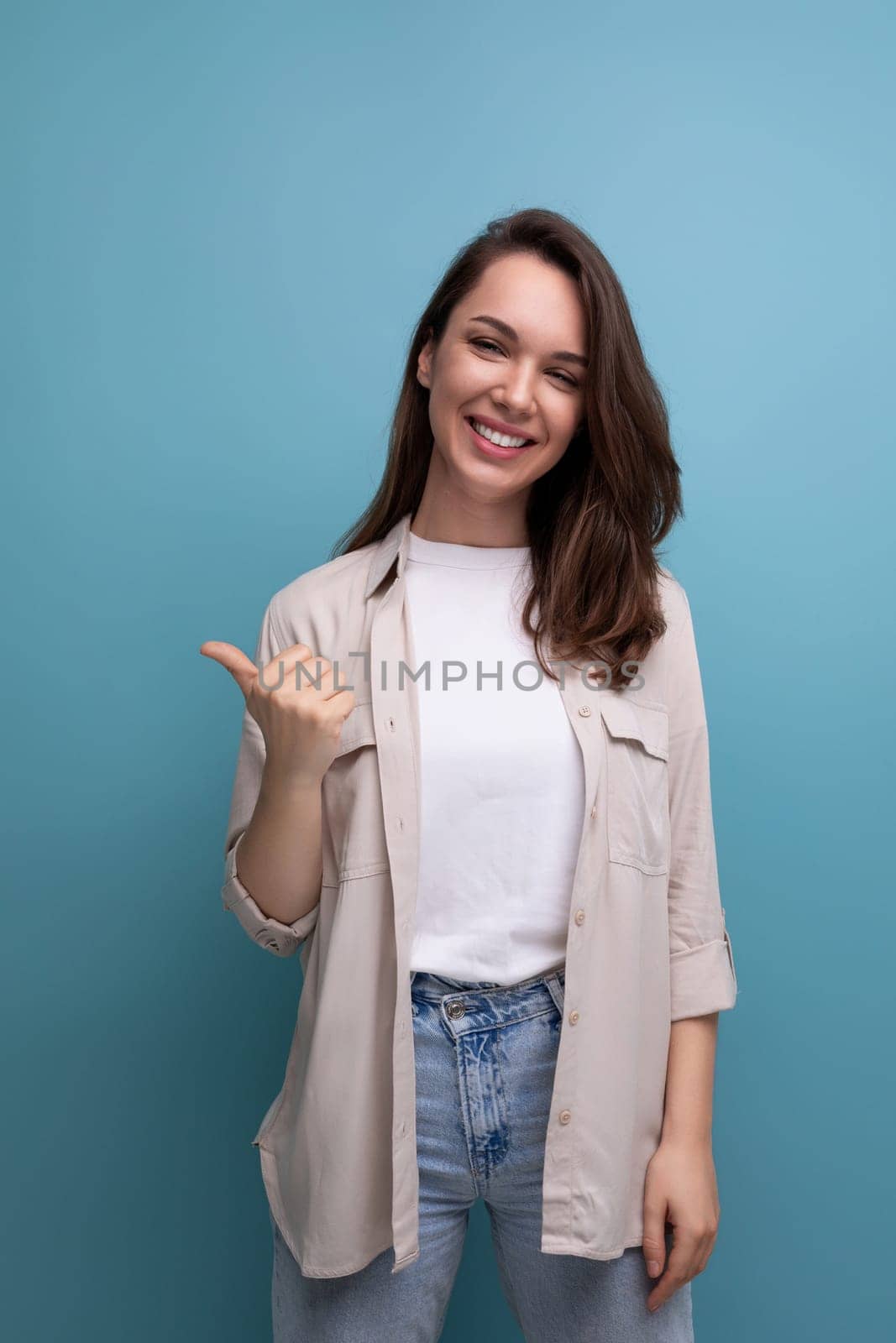 smiling brunette young woman in shirt and jeans on blue background.