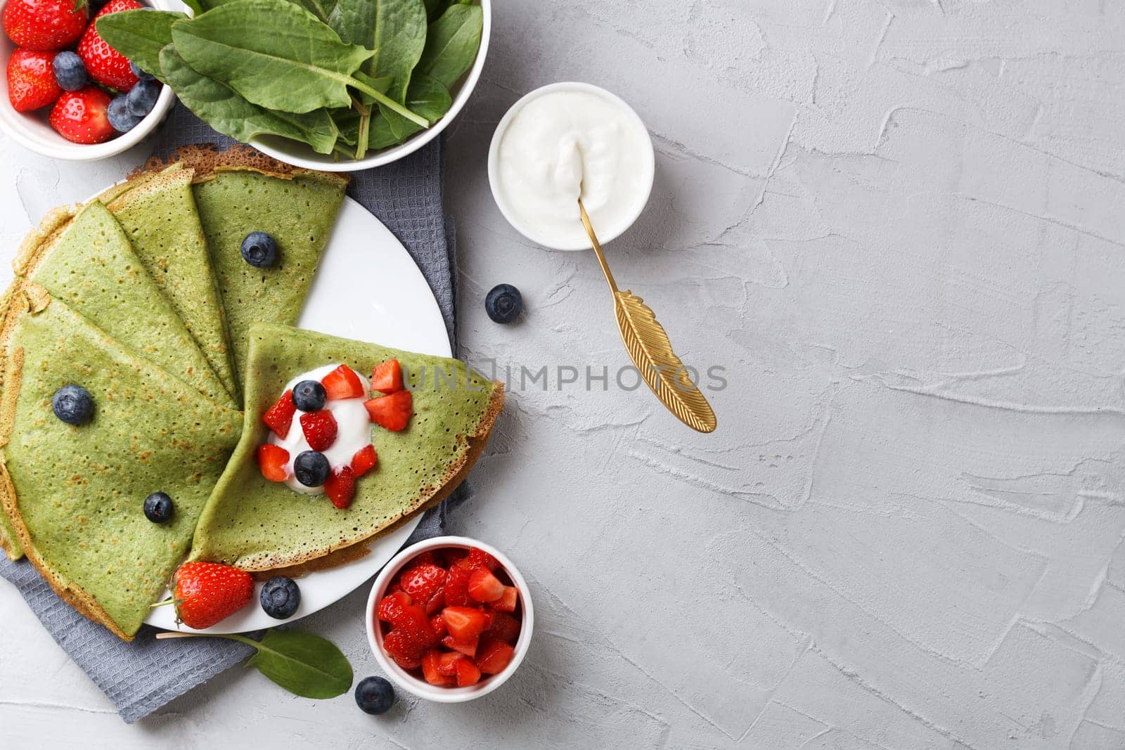 Green pancakes with spinach on a plate with fresh berries and sour cream, on a gray background with textiles. copy space by lara29