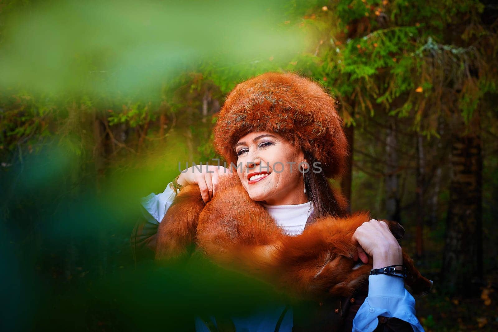 Girl in a leather jacket, a big red fox fur hat and with the skin of a fox killed on the hunt in the forest in autumn. A female model poses as fabulous royal huntress on nature hunt at photo shoot