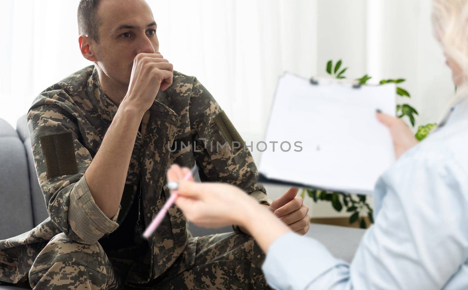 sad soldier with ptsd talking at psychiatrist and gesturing while sitting on couch during therapy session.