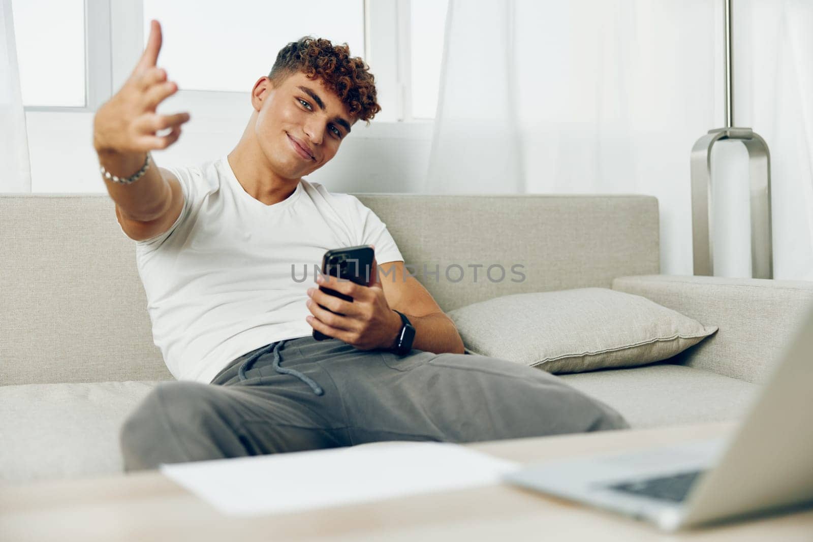 man interior curly couch using cellphone message communication person selfies sports online young smart smartphone