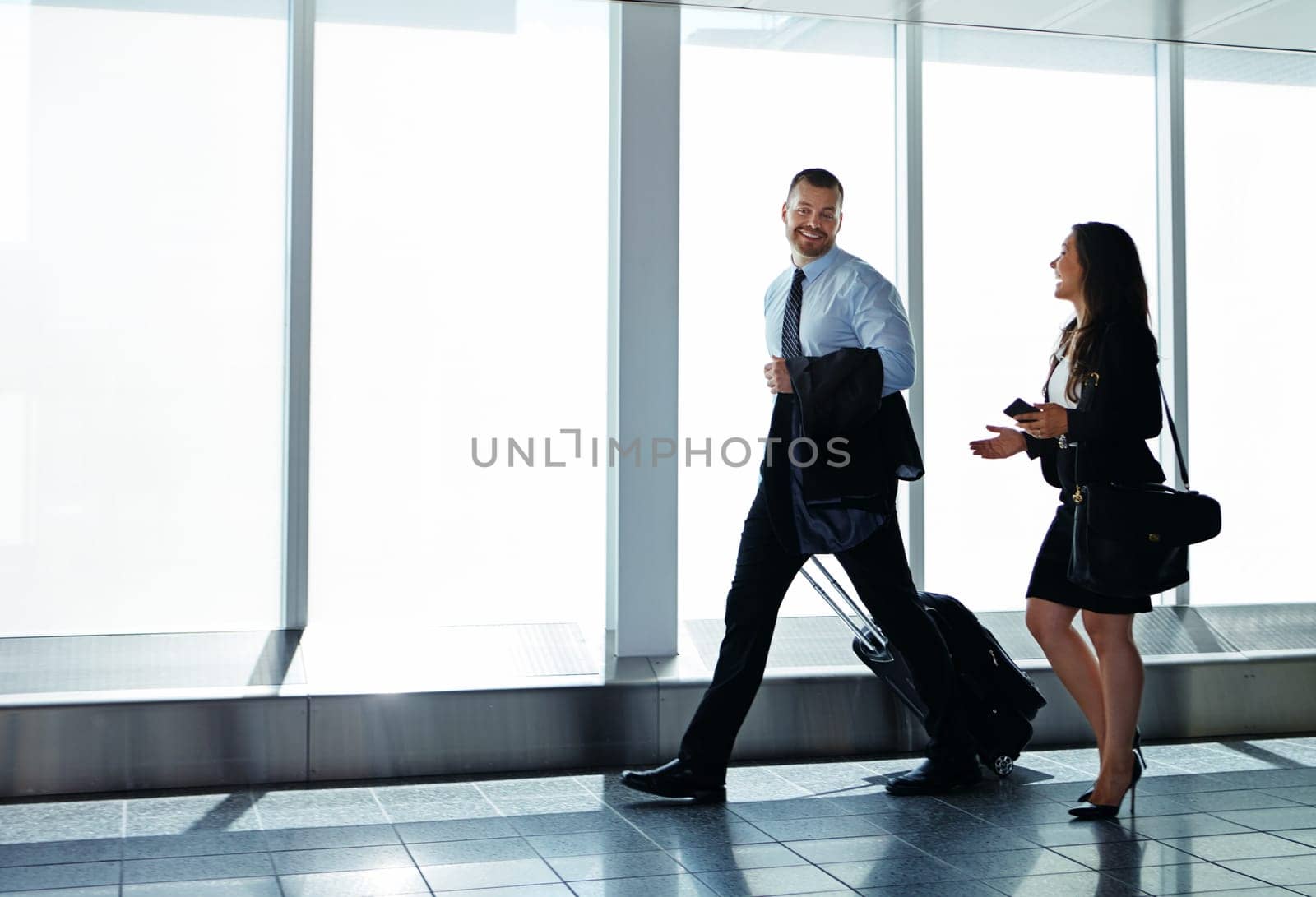 They make great business travel companions. two businesspeople talking together while walking through an airport