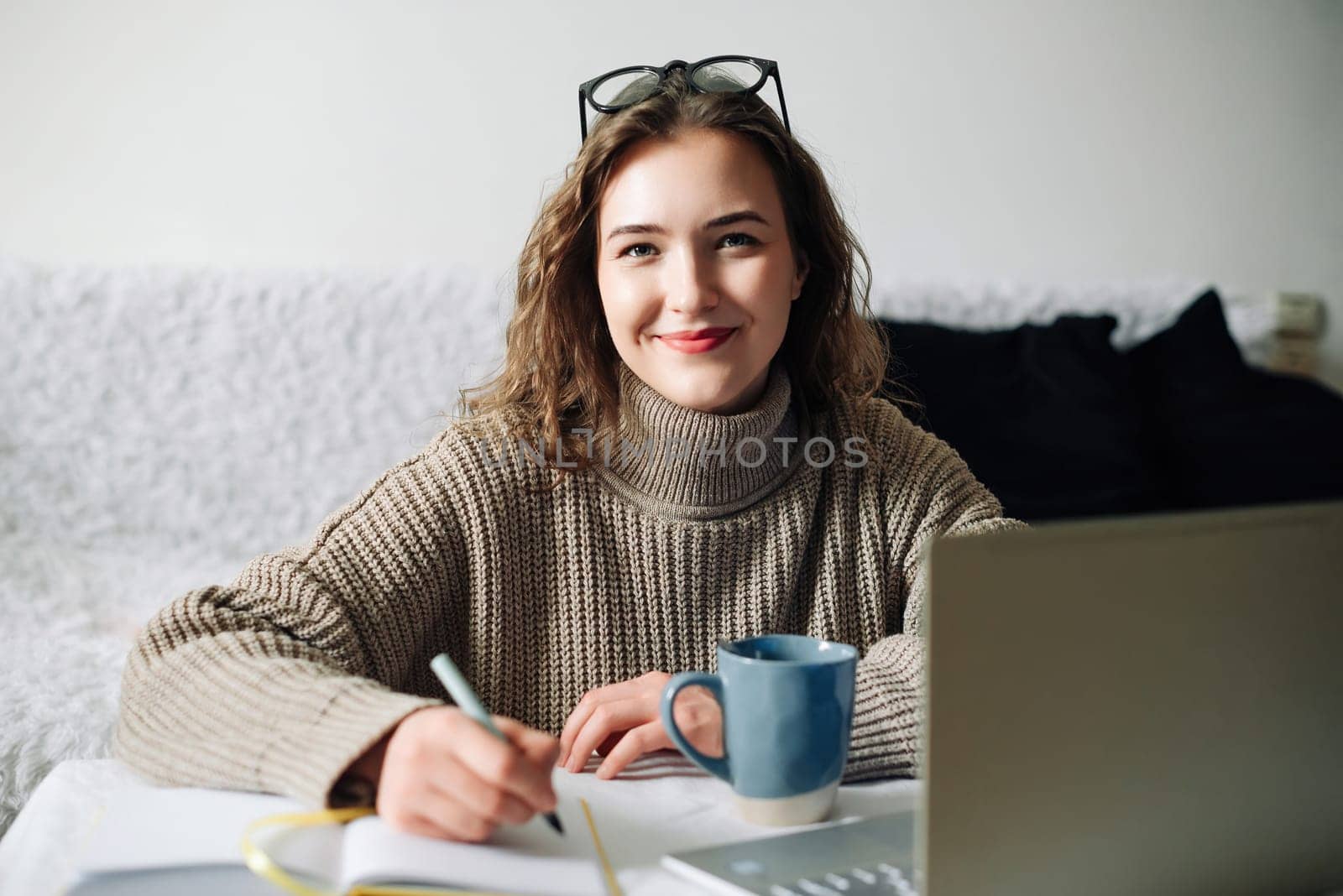 Home office of a young female English tutor with laptop, coffee, and notes, preparing for online lesson with student, sitting at kitchen table. Educator working remotely from home