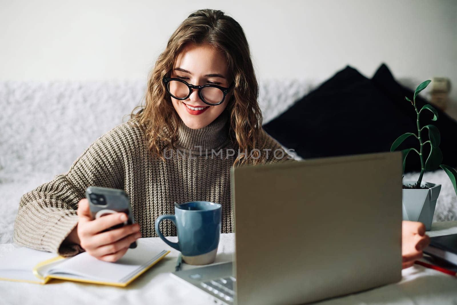 SMM specialist working from home at kitchen table, using smartphone to select blogger for product promotion in social media, in front of laptop. Influencer marketing concept.