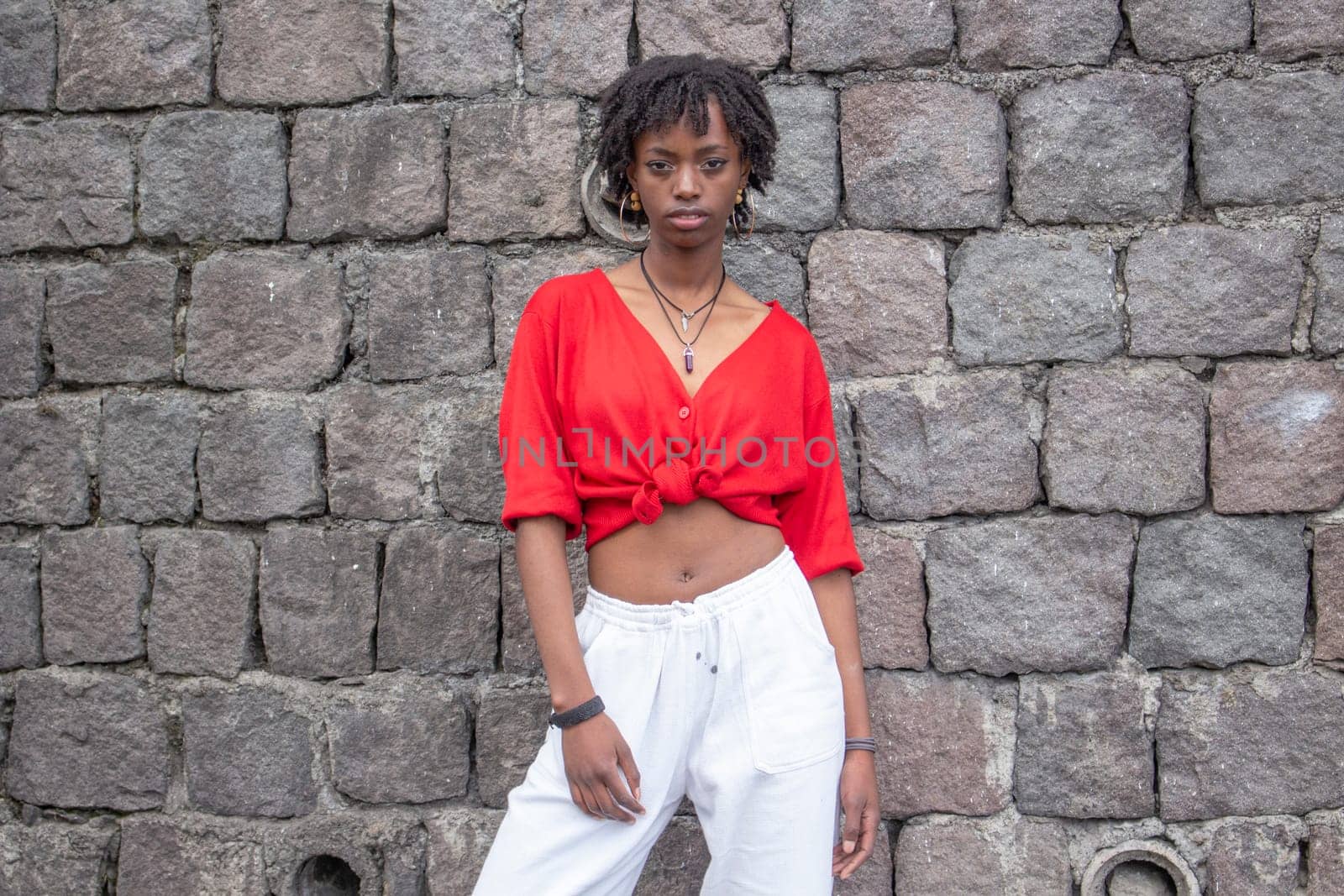 sexy black girl with red sweater and white pants modeling on a street wall. High quality photo