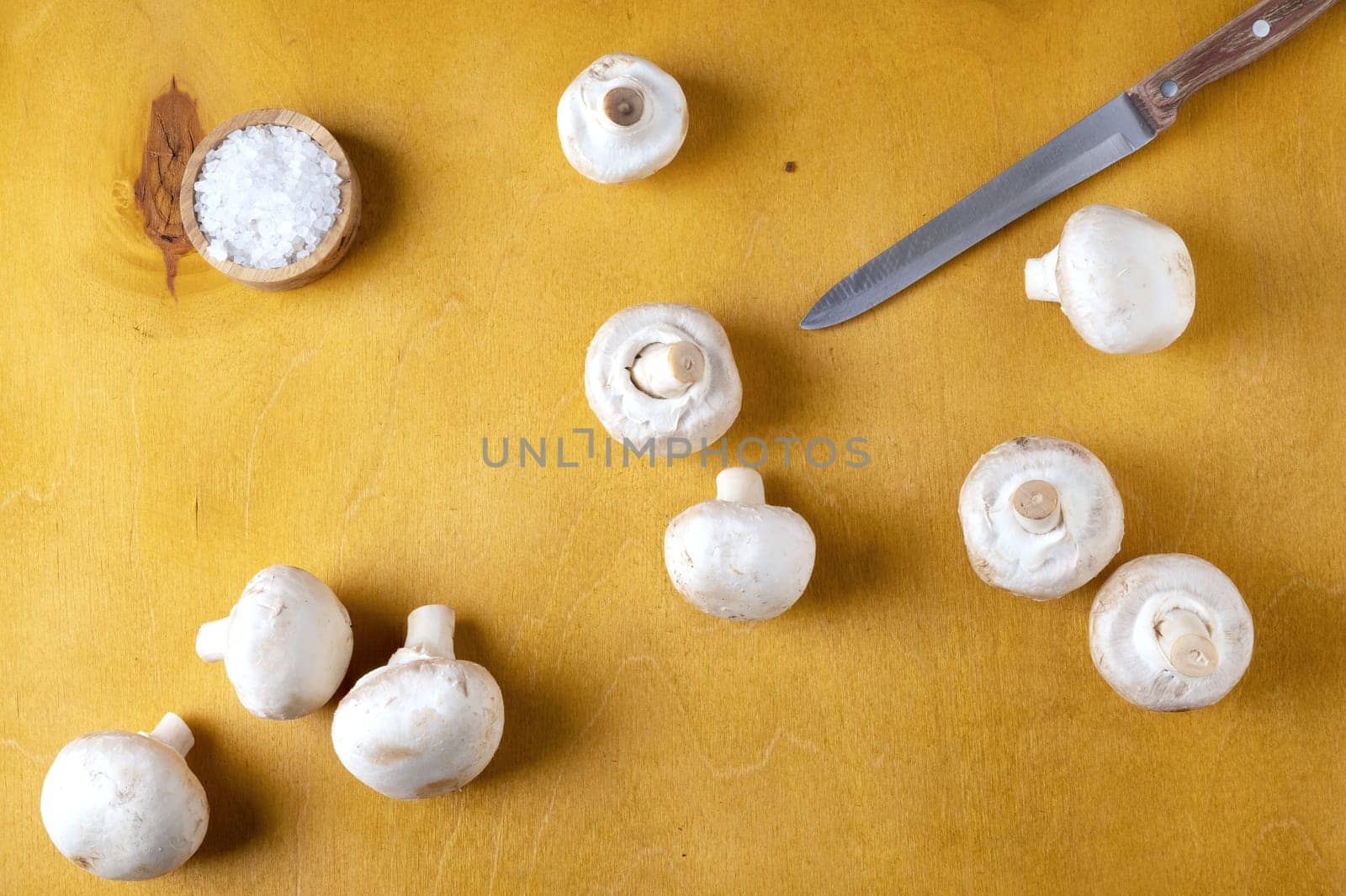 Close-up of champignon mushrooms and a kitchen knife on a yellow background. Selective focus.