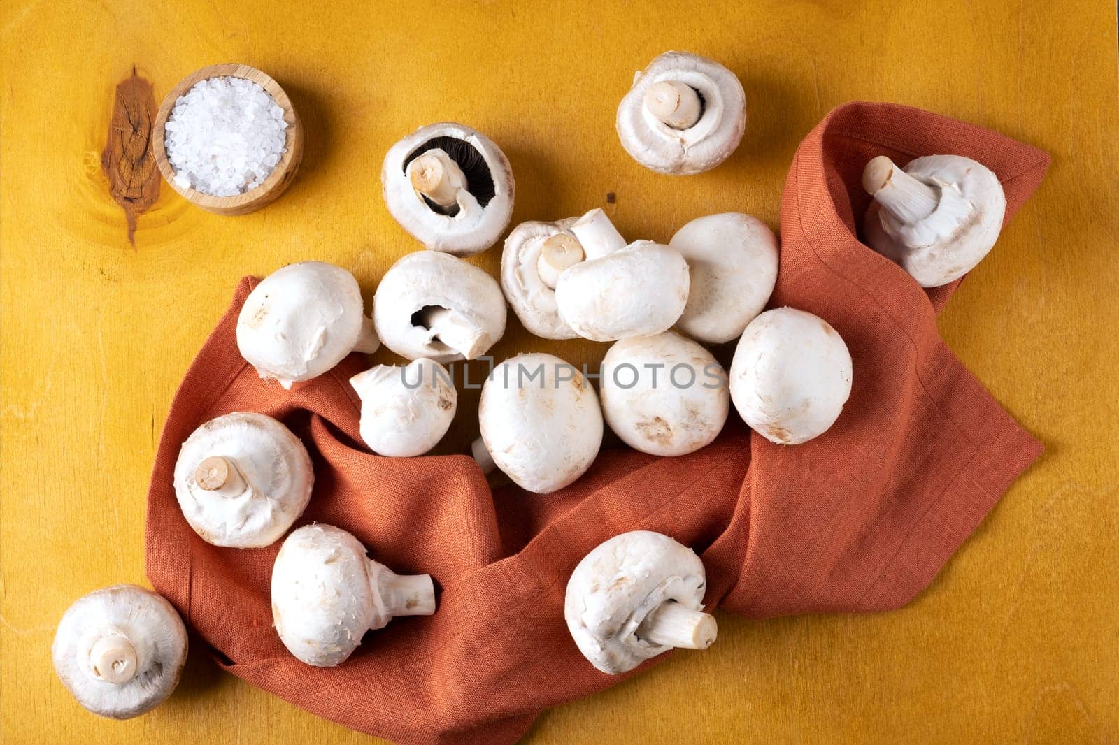 Close-up of champignon mushrooms on a linen napkin on a yellow background. Selective focus.
