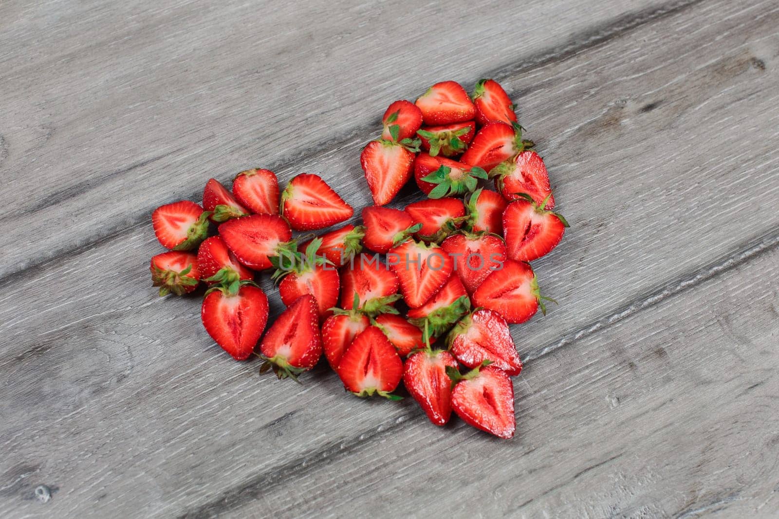 Strawberries cut in half, arranged to shape of heart, placed on gray wood desk. by Ivanko