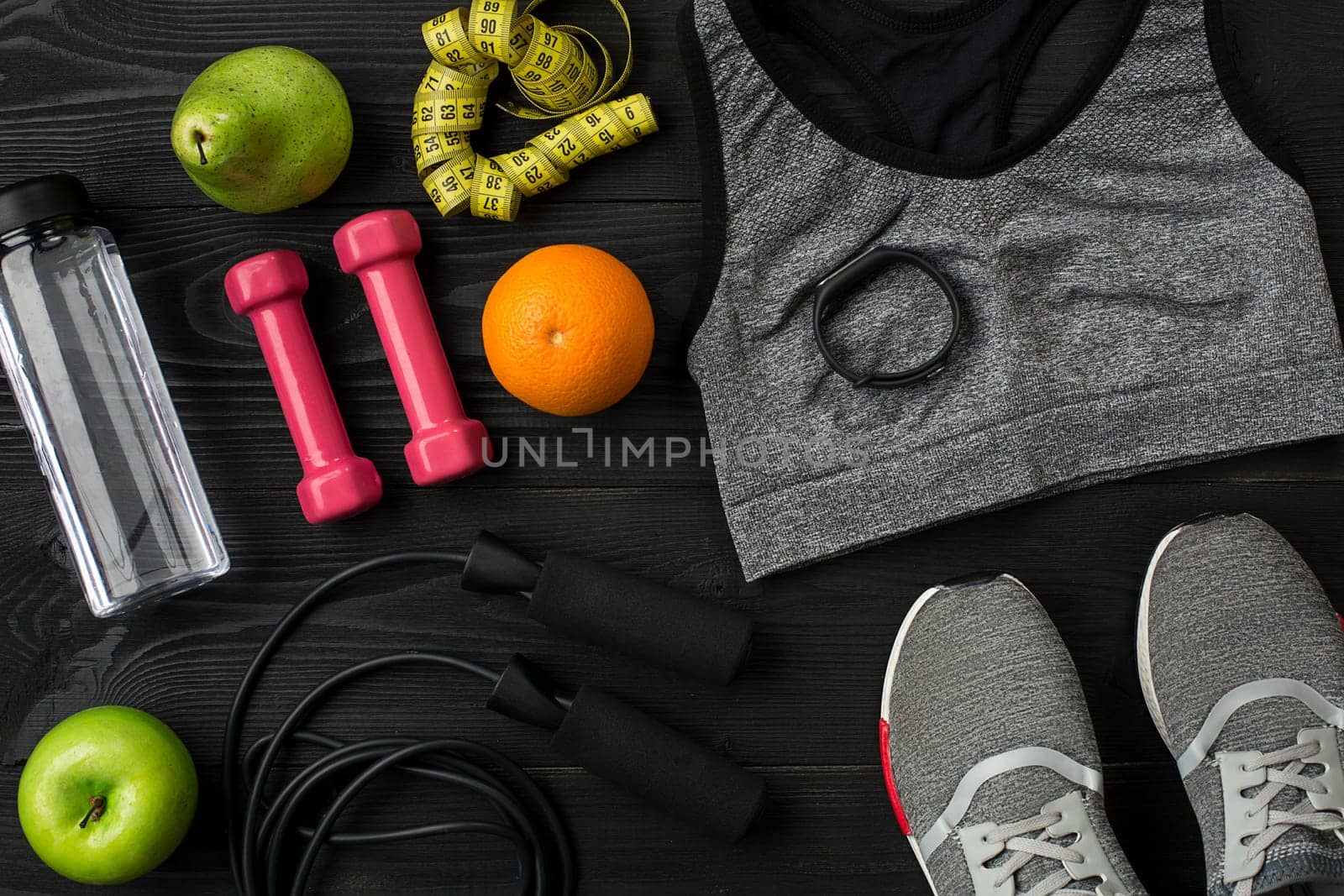 Athlete's set with female clothing, sneakers and bottle of water on dark background. Top view. Copy space. Still life. Ideal for sporty blog.