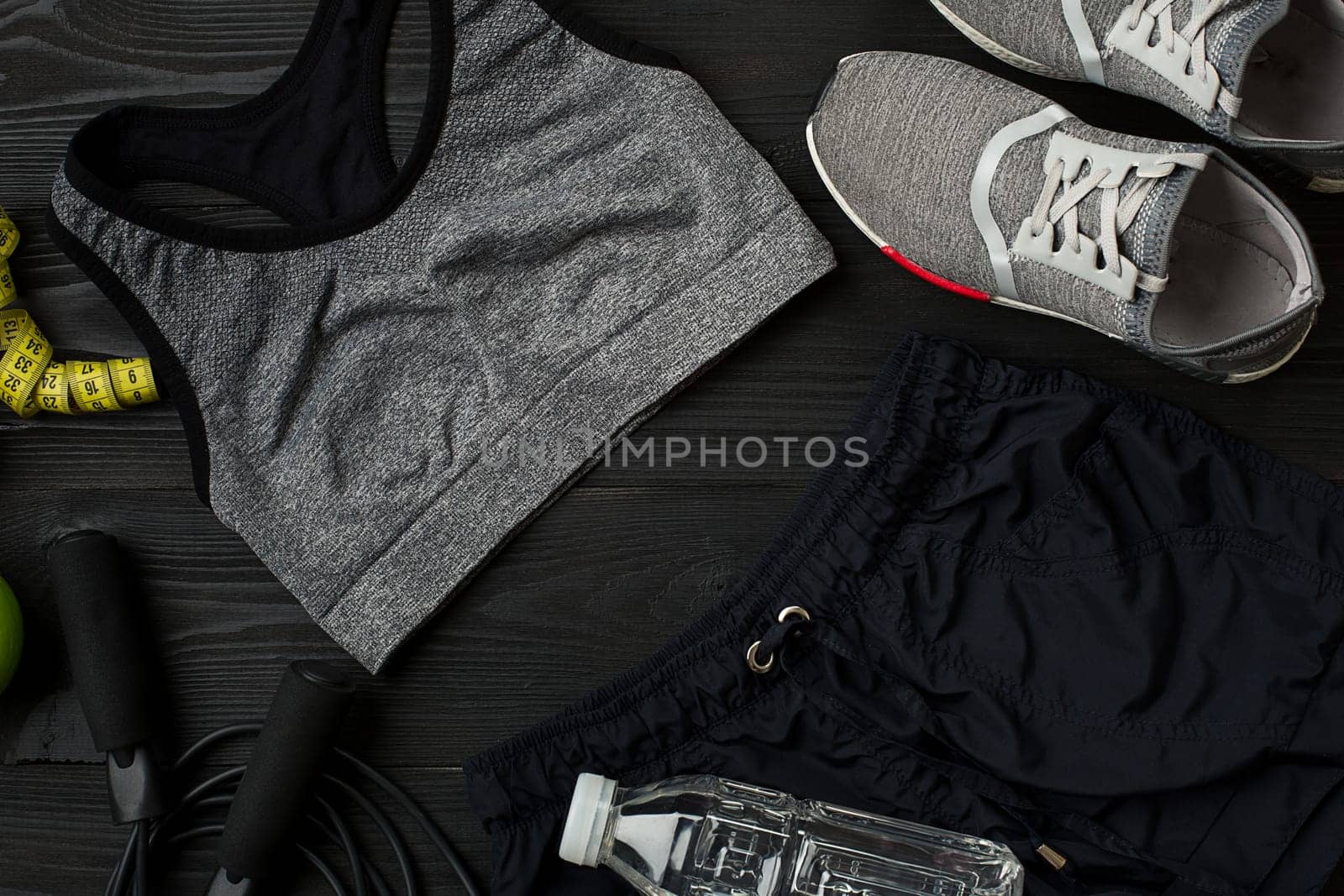 Athlete's set with female clothing, sneakers and bottle of water on dark background. Top view. Copy space. Still life. Ideal for sporty blog.