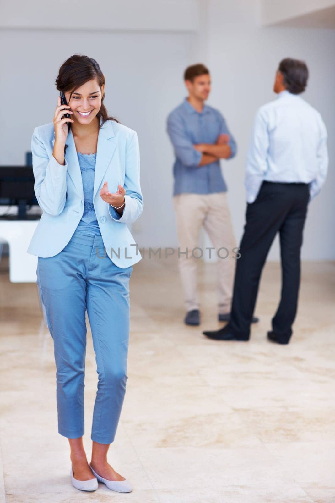 Business woman speaking on cellphone. Full length of happy business woman speaking on cellphone with colleagues in background