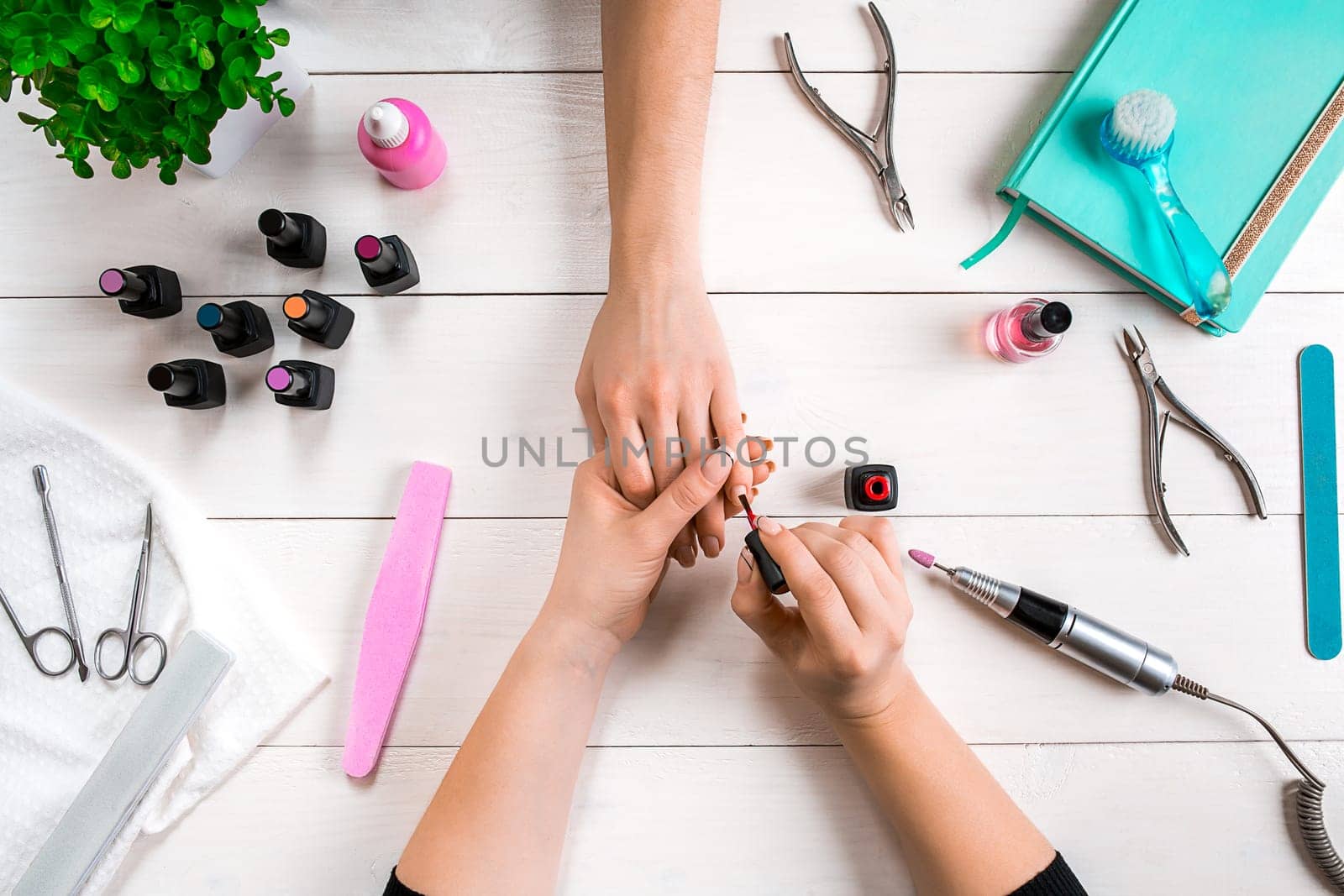 Nail care. Closeup of female hands filing nails with professional nail file in beauty nail salon. Close-up of beautician hands doing perfect manicure on woman's hands. Nail hygiene. Top view