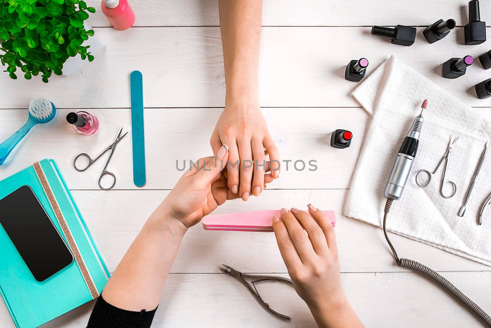 Manicure for the client. Close-up of the hands of a manicurist and client on a wooden background. Nail care. Manicure set and nail polish.