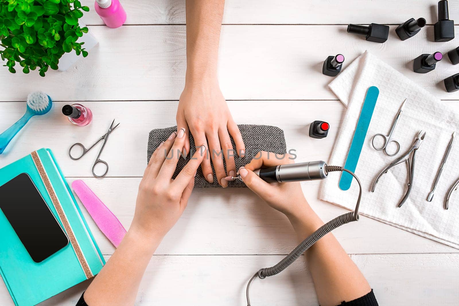 Nail care. Closeup of female hands filing nails with professional nail file in beauty nail salon. Close-up of beautician hands doing perfect manicure on woman's hands. Nail hygiene. Top view