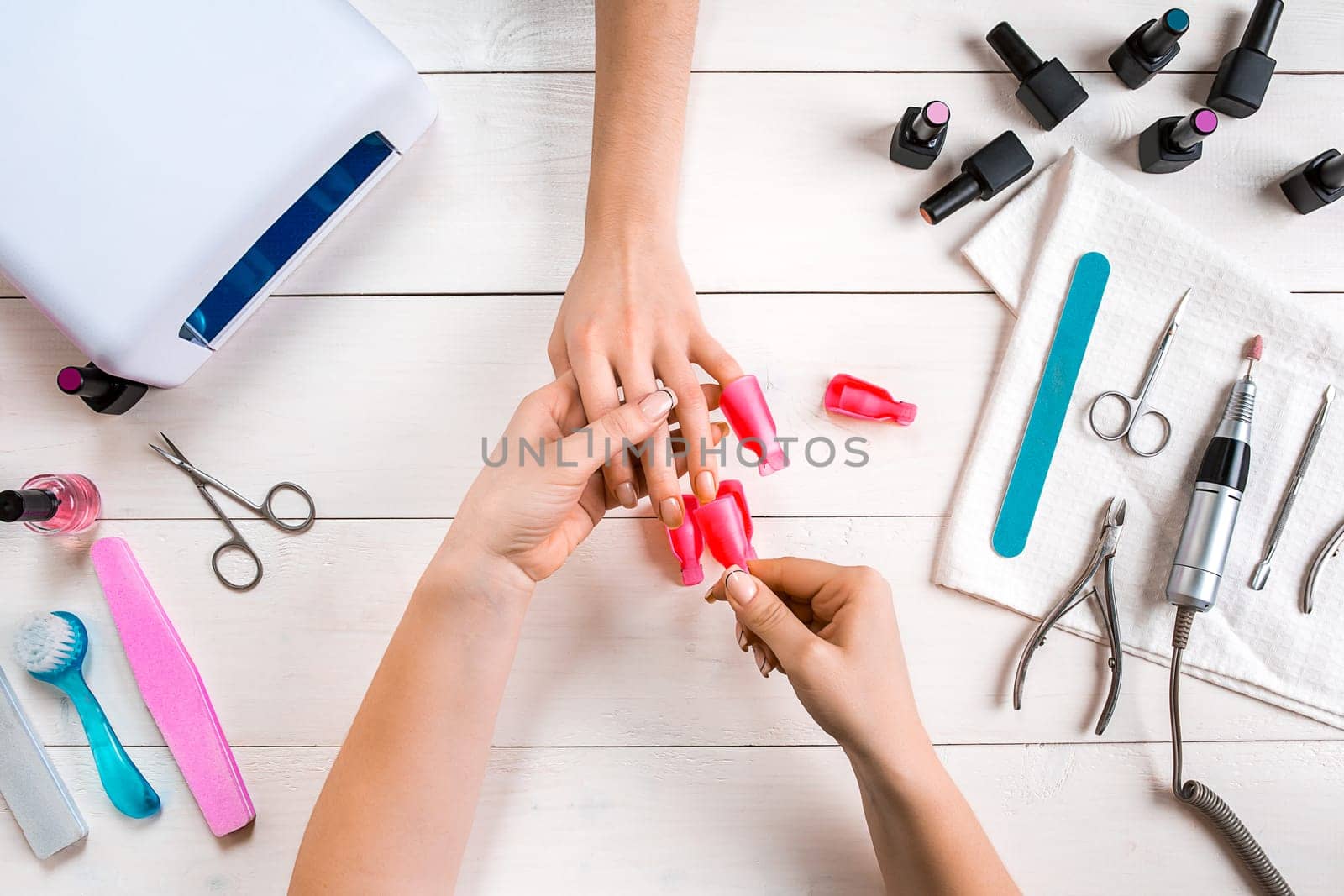 Nail care. Closeup of female hands filing nails with professional nail file in beauty nail salon. Close-up of beautician hands doing perfect manicure on woman's hands. Nail hygiene. Top view