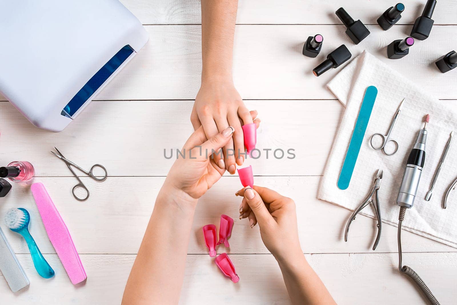 Nail care. Closeup of female hands filing nails with professional nail file in beauty nail salon. Close-up of beautician hands doing perfect manicure on woman's hands. Nail hygiene. Top view