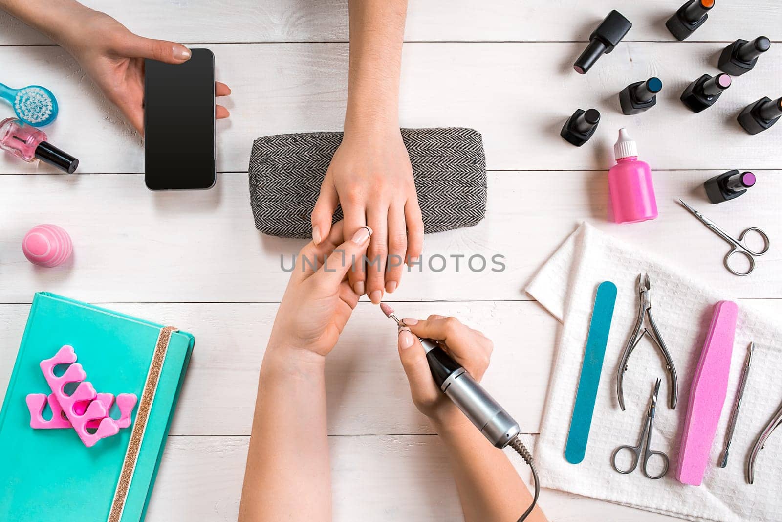 Closeup shot of a woman in a nail salon receiving a manicure by a beautician with nail file. Woman getting nail manicure. Beautician file nails to a customer.