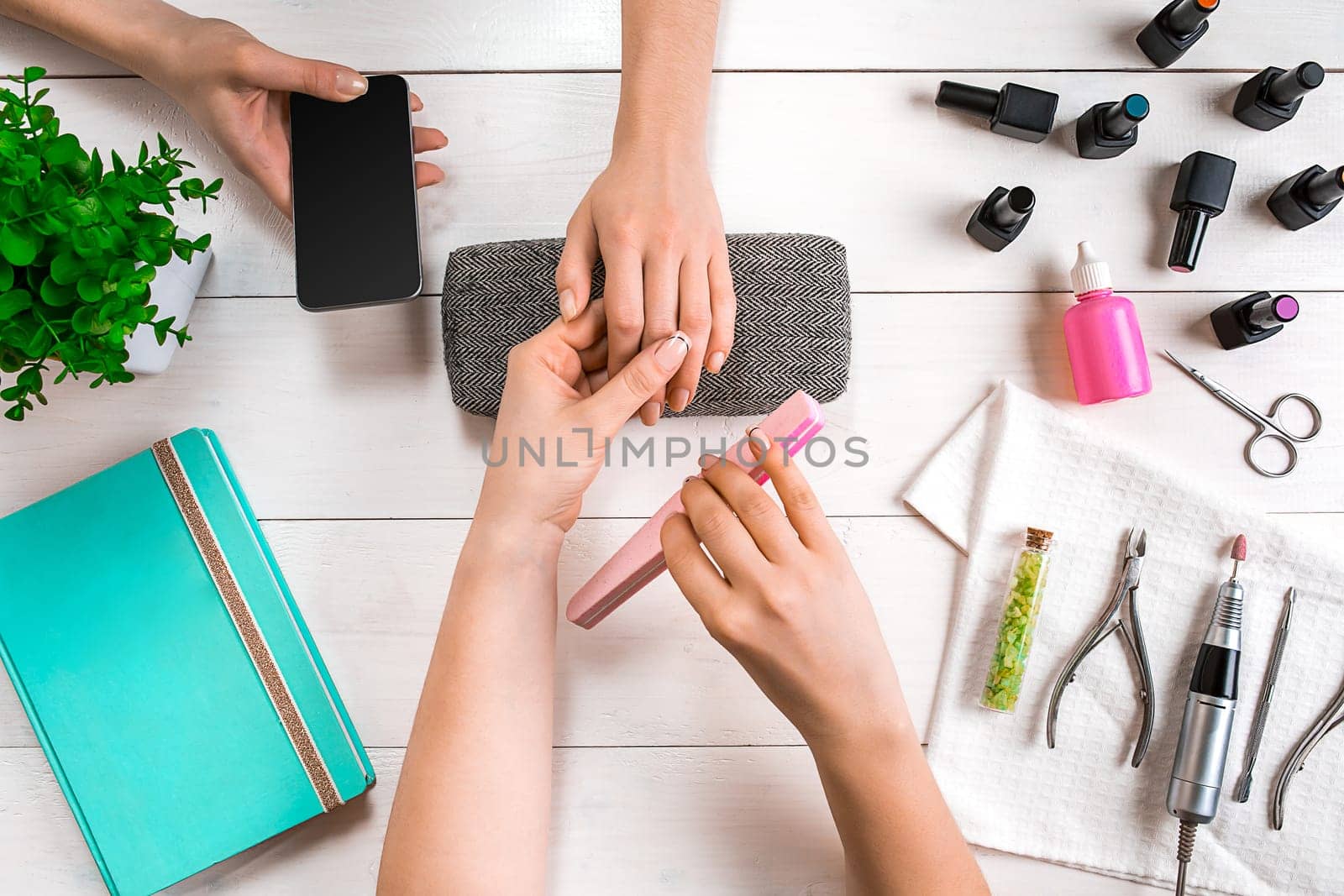 Manicure for the client. Close-up of the hands of a manicurist and client on a wooden background. Nail care. Manicure set and nail polish.