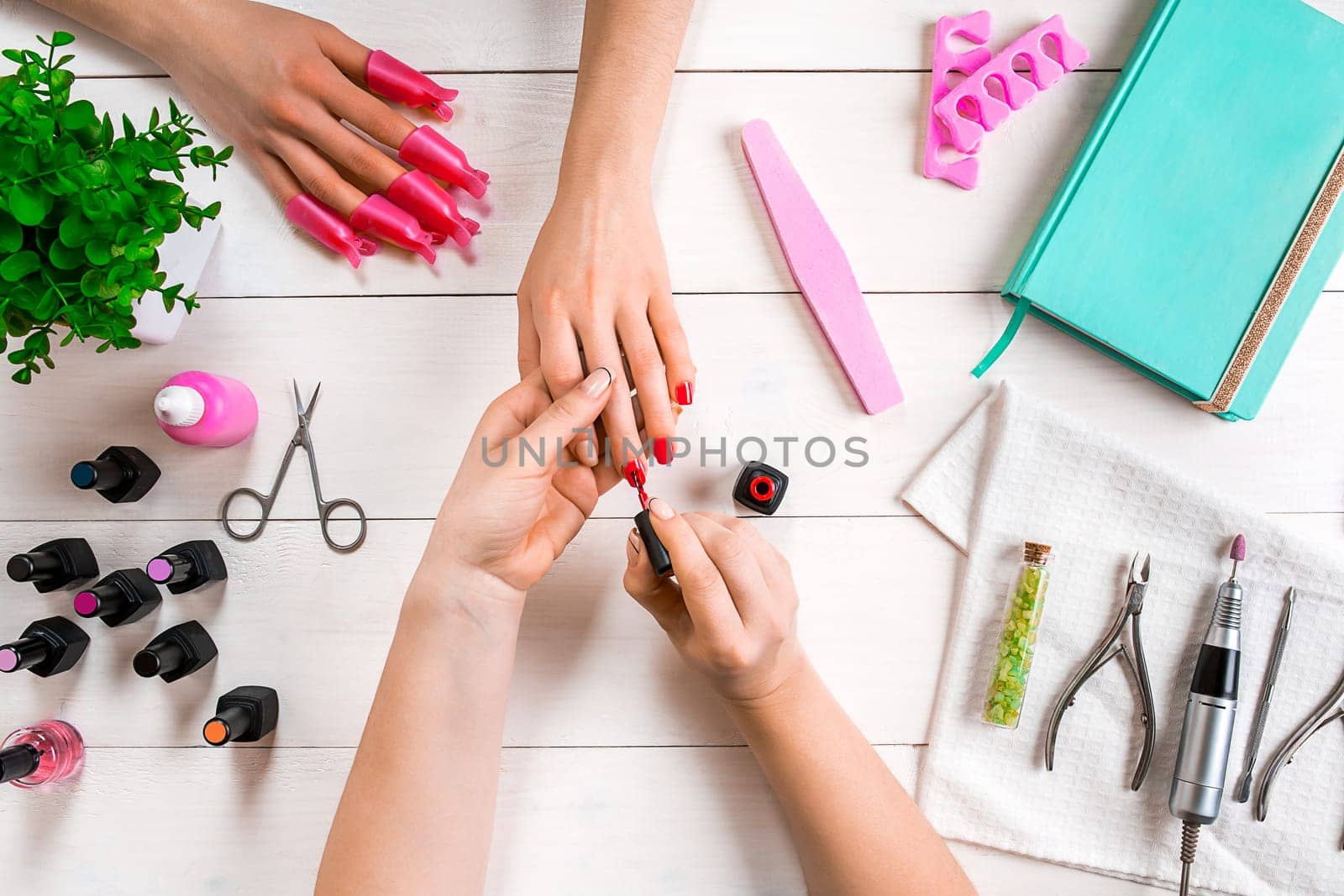 Nail care. Closeup of female hands filing nails with professional nail file in beauty nail salon. Close-up of beautician hands doing perfect manicure on woman's hands. Nail hygiene. Top view