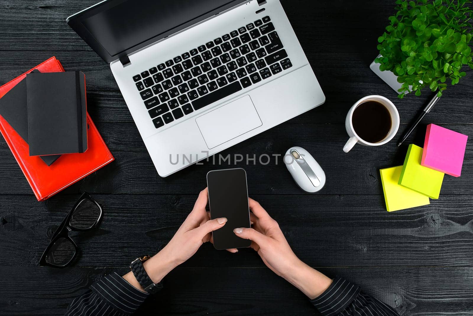 Mix of office supplies and gadgets on a wooden desk background. View from above. Female hands on the laptop keyboard