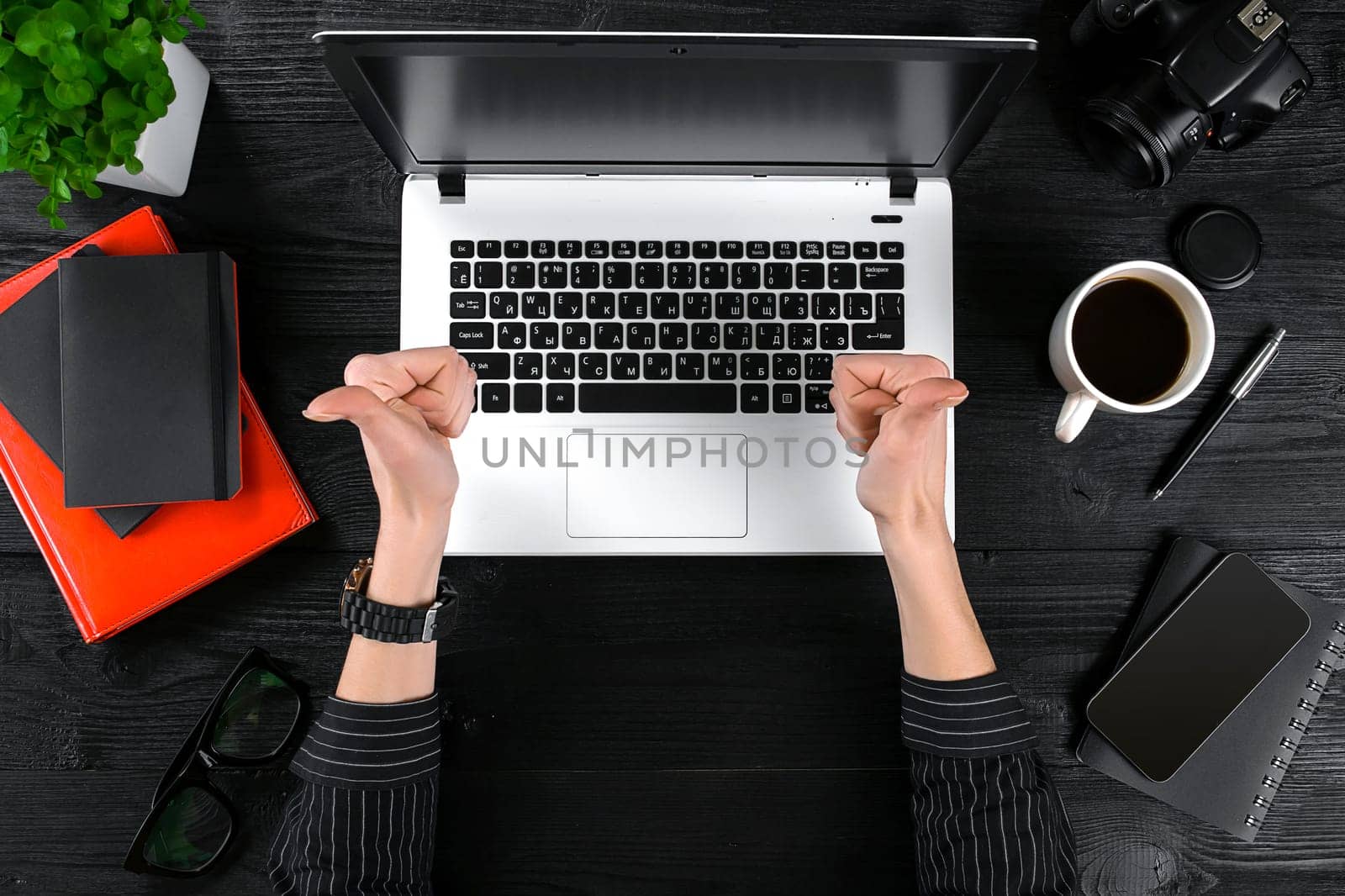 Woman working at the office table. Top view of human hands, laptop keyboard, a cup of coffee, smartphone, notebook and a flower on a wooden table background. Woman showing thumbs up