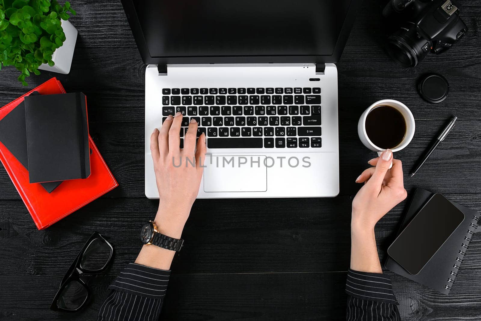 Mix of office supplies and gadgets on a wooden desk background. View from above. Female hands on the laptop keyboard