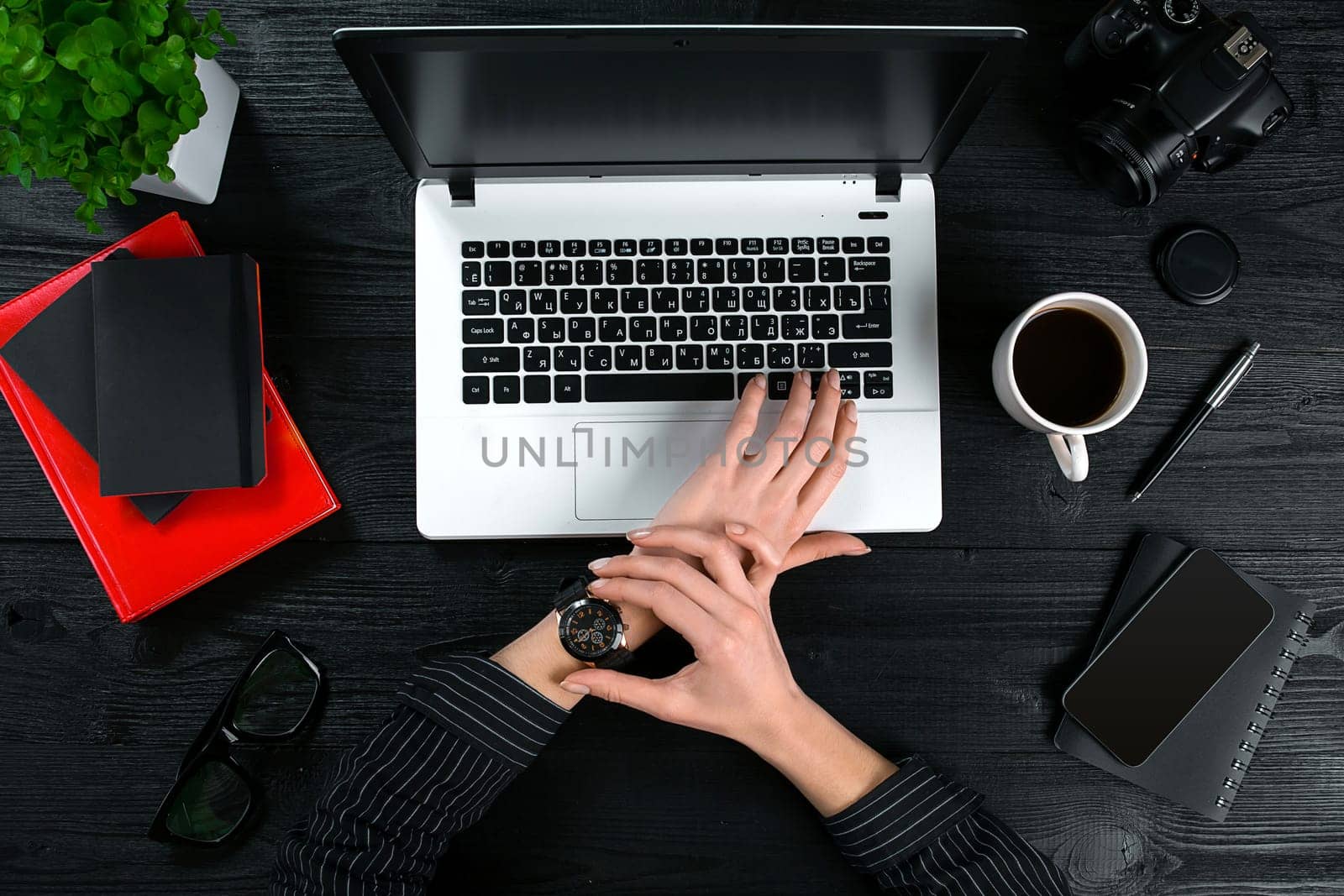 Mix of office supplies and gadgets on a wooden desk background. View from above. Female hands on the laptop keyboard