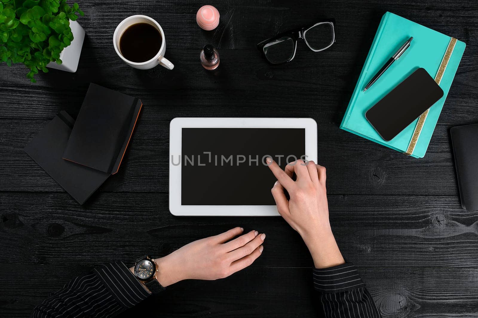 Mix of office supplies and gadgets on a wooden desk background. View from above. In the female hands of a tablet