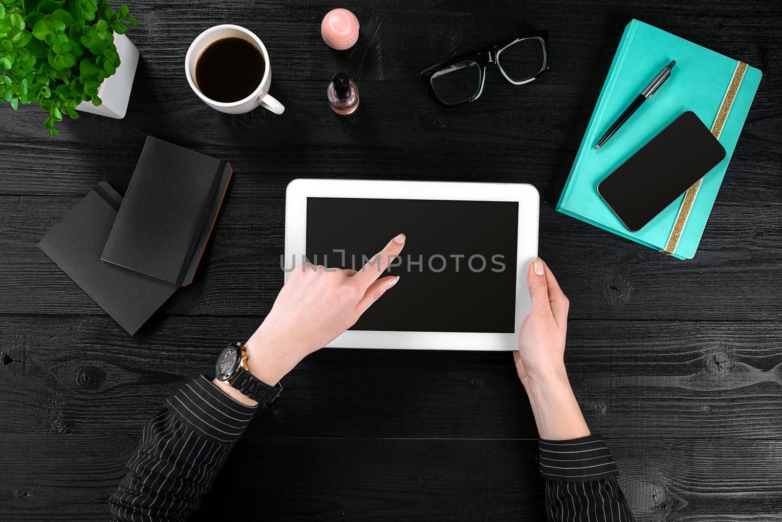 Mix of office supplies and gadgets on a wooden desk background. View from above. In the female hands of a tablet