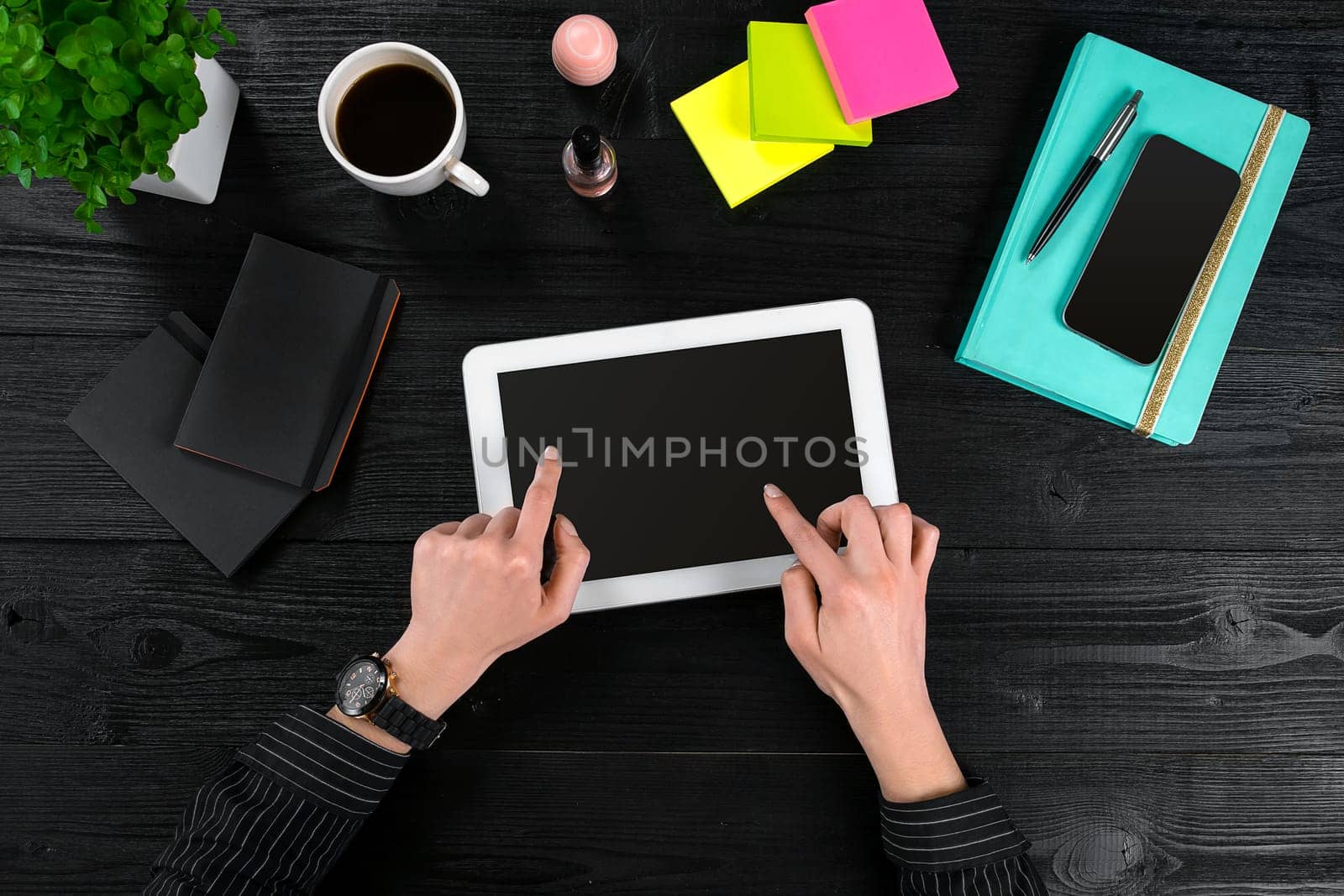Mix of office supplies and gadgets on a wooden desk background. View from above. In the female hands of a tablet