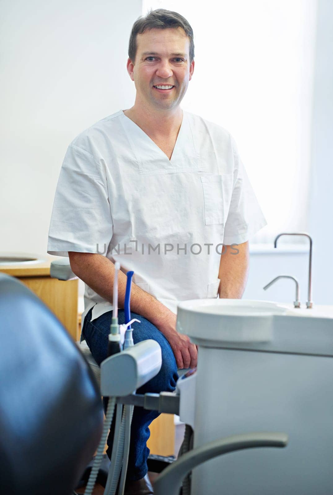 Your friendly dentist. Portrait of a male dentist sitting by the dental equipment in his office. by YuriArcurs