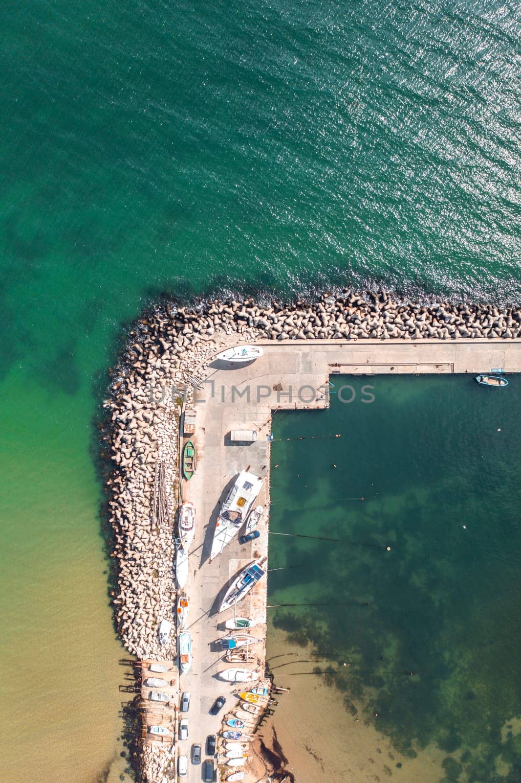 Aerial top-down view of fishing pier with fishing boats and docked sailboats on dry land. Sea pier and sea city