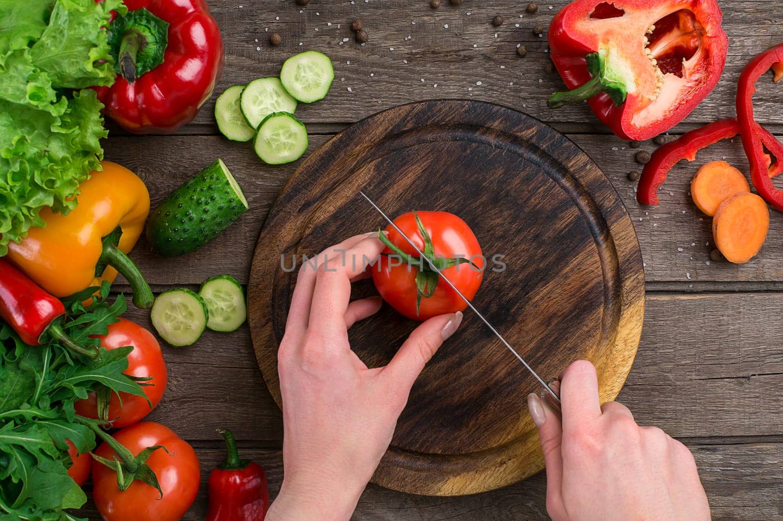 Sport and diet. Sliced Vegetables. Peppers, tomatoes, salad on rustic background. Top view. Copy space. Hands that cut a tomato on a board