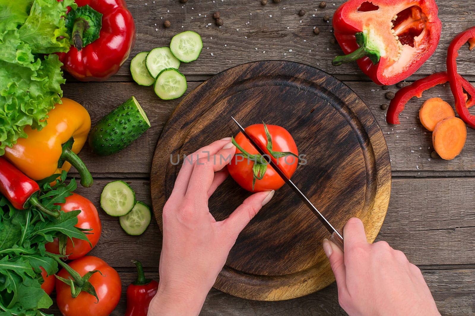 Female hands cutting tomato at table, top view. On the table vegetables and a wooden board