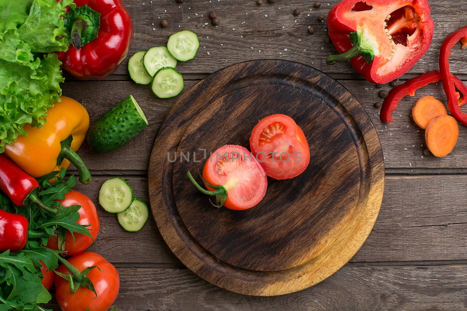 Cut tomato on a wooden board and vegetables on a table. Copy space. Top view
