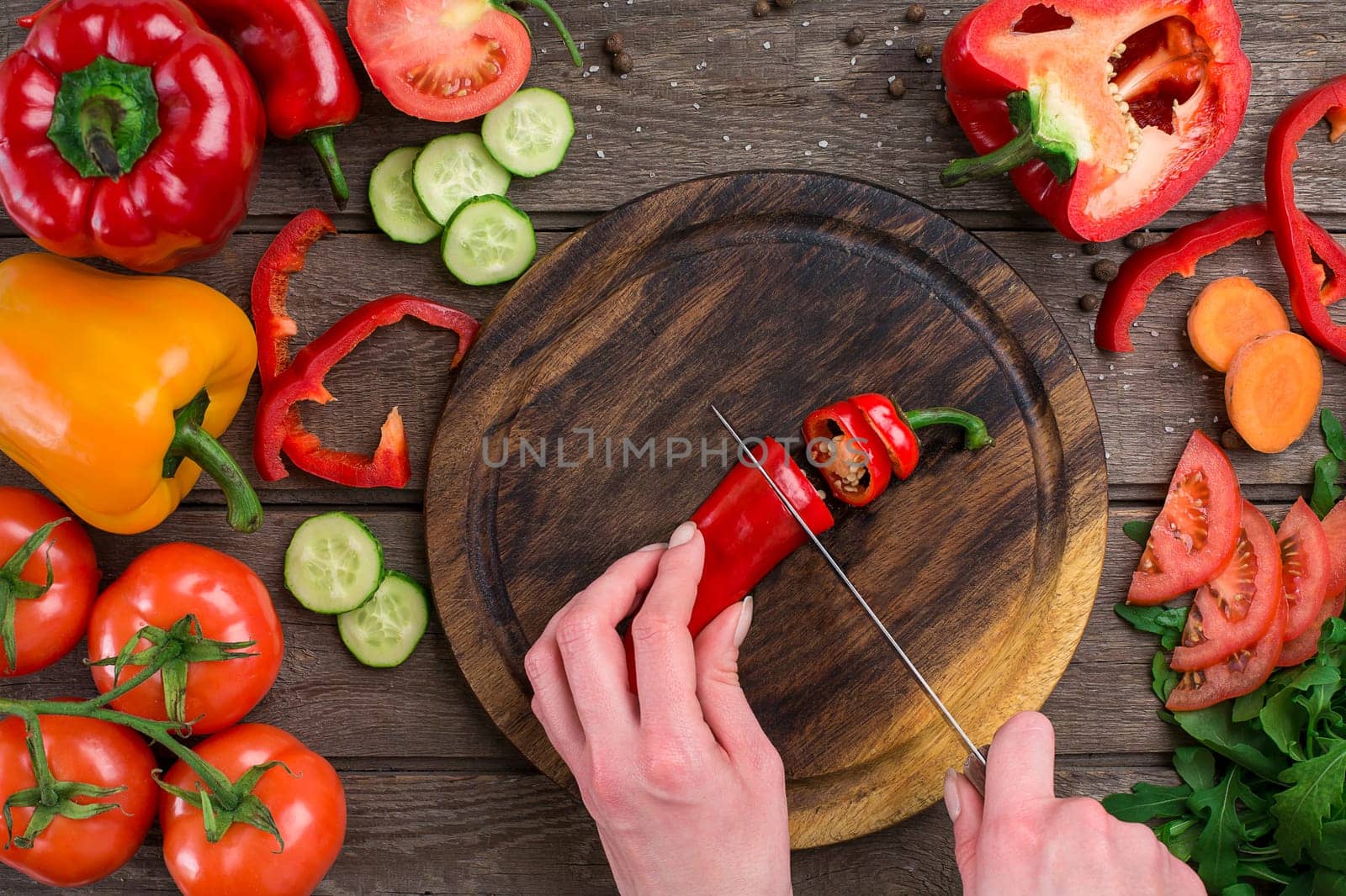 Female hands cutting hot peppers at table, top view. On the table vegetables and a wooden board