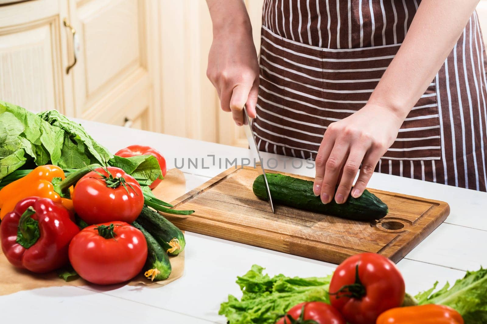 Young woman cooking in the kitchen at home. A woman cuts a cucumber and vegetables with a knife. by nazarovsergey