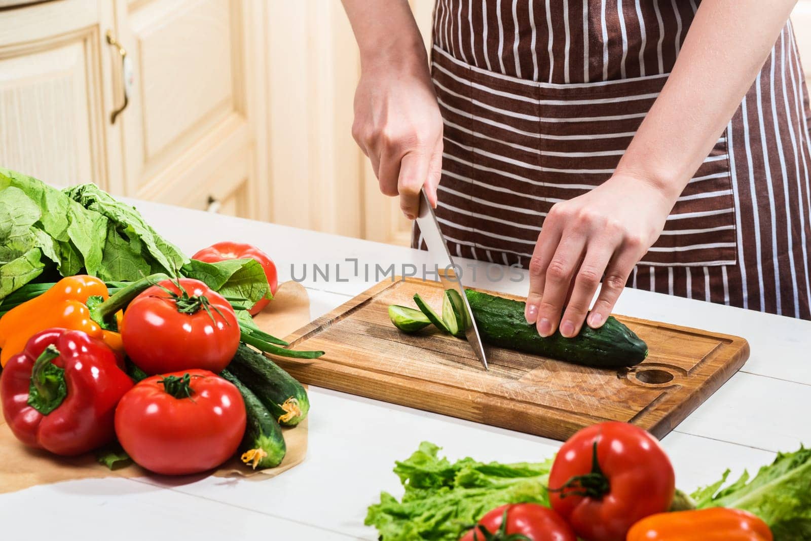 Young woman cooking in the kitchen at home. A woman cuts a cucumber and vegetables with a knife. by nazarovsergey