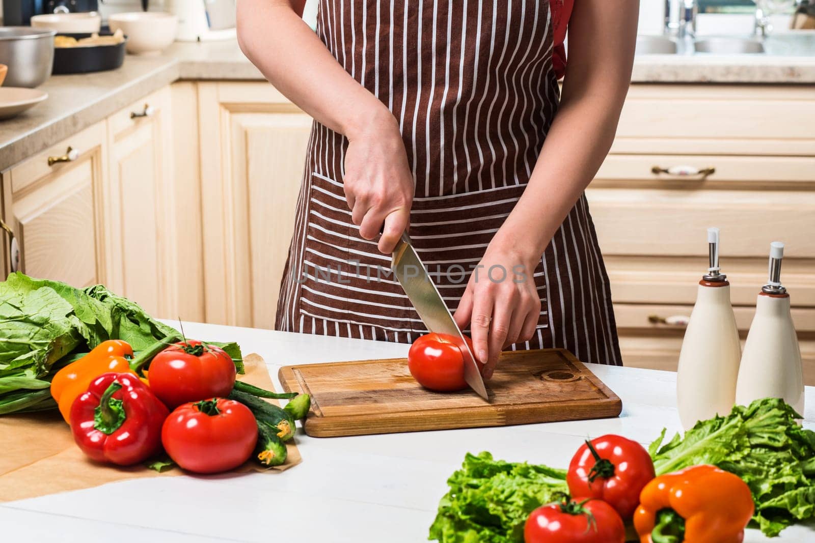 Young woman cooking in the kitchen at home. A woman cuts a tomato and vegetables with a knife. by nazarovsergey