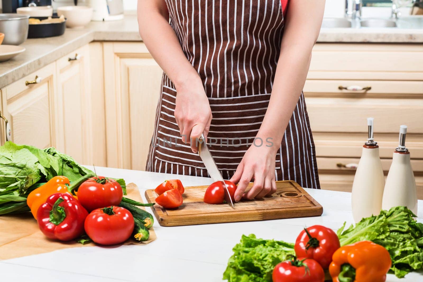 Young woman cooking in the kitchen at home. A woman cuts a tomato and vegetables with a knife. by nazarovsergey