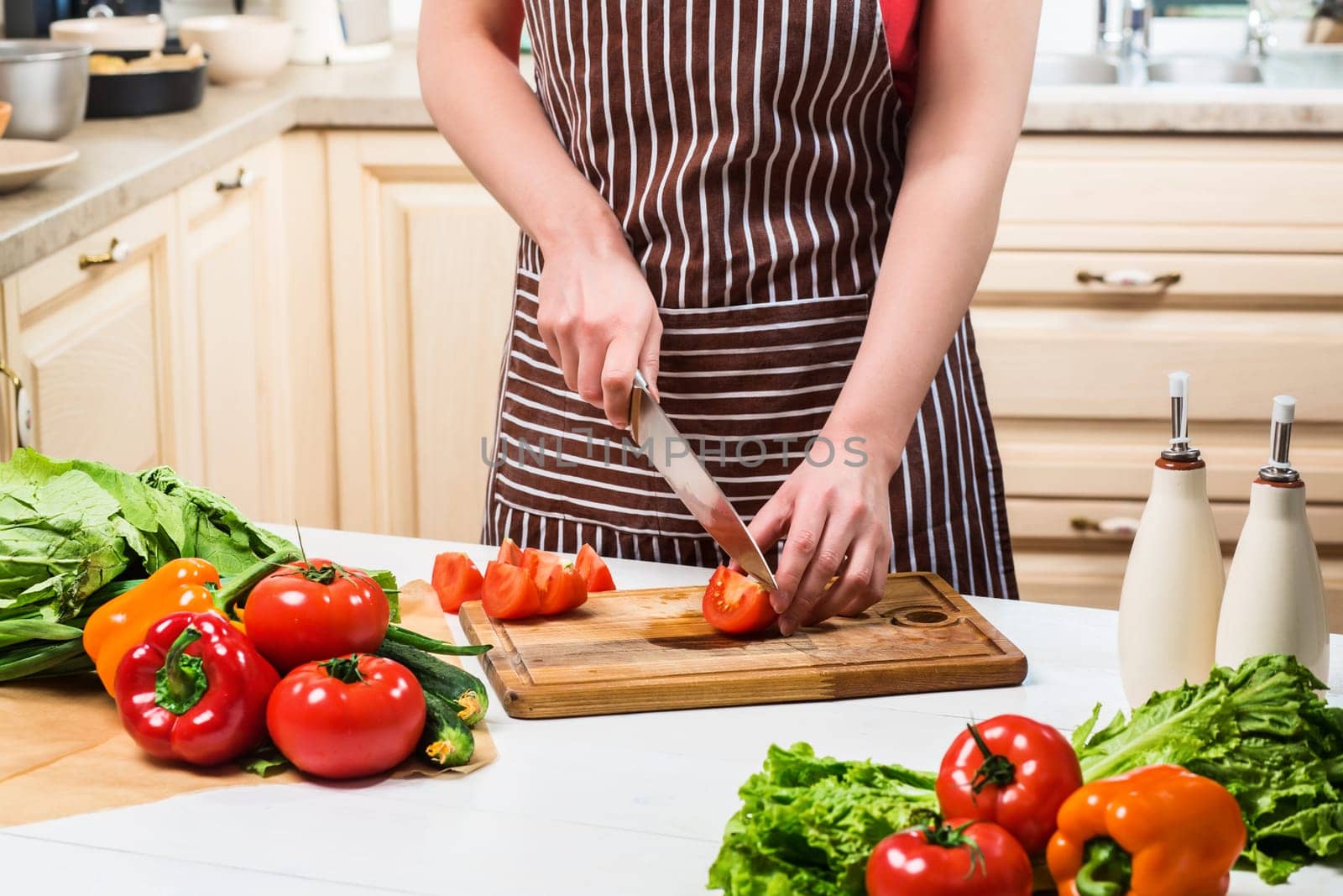 Young woman cooking in the kitchen at home. A woman cuts a tomato and vegetables with a knife. by nazarovsergey