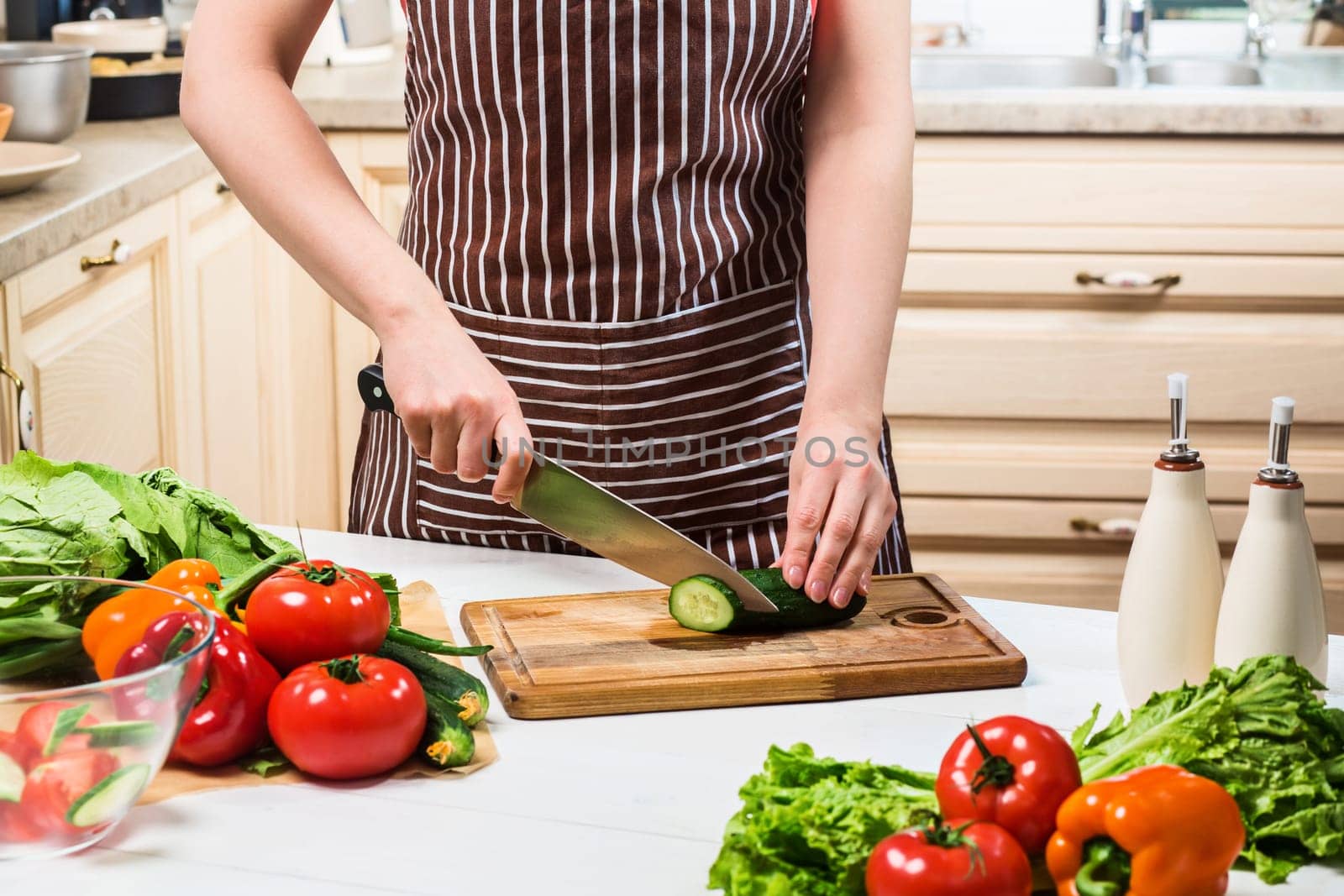 Young woman cooking in the kitchen at home. A woman cuts a cucumber and vegetables with a knife. by nazarovsergey