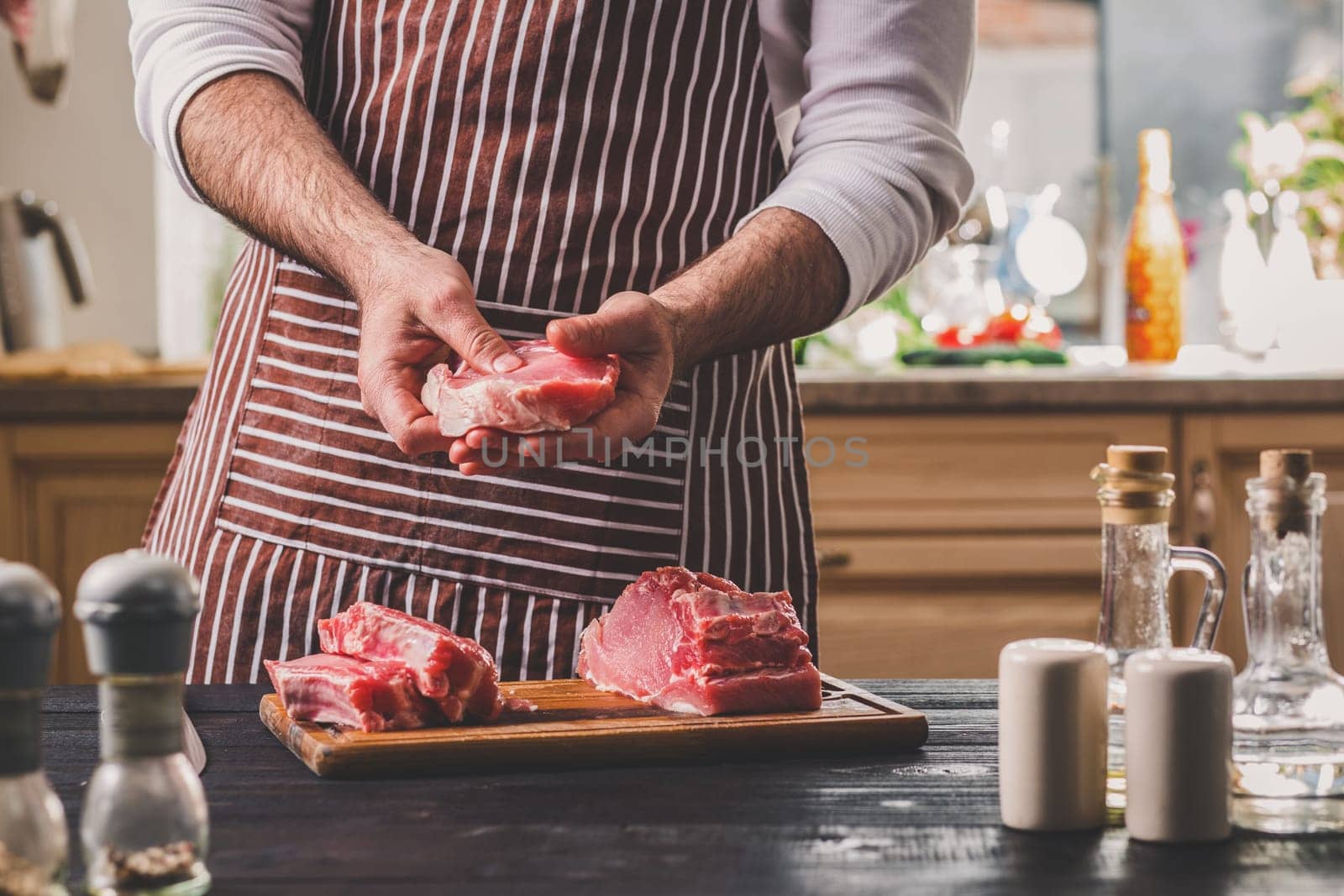 Preparation of dinner. Cooking, processing of meat beef, tenderloin . Person man's hands marinates meat - sprinkles with salt, pepper. Black wooden table, spices and herbs in the frame.
