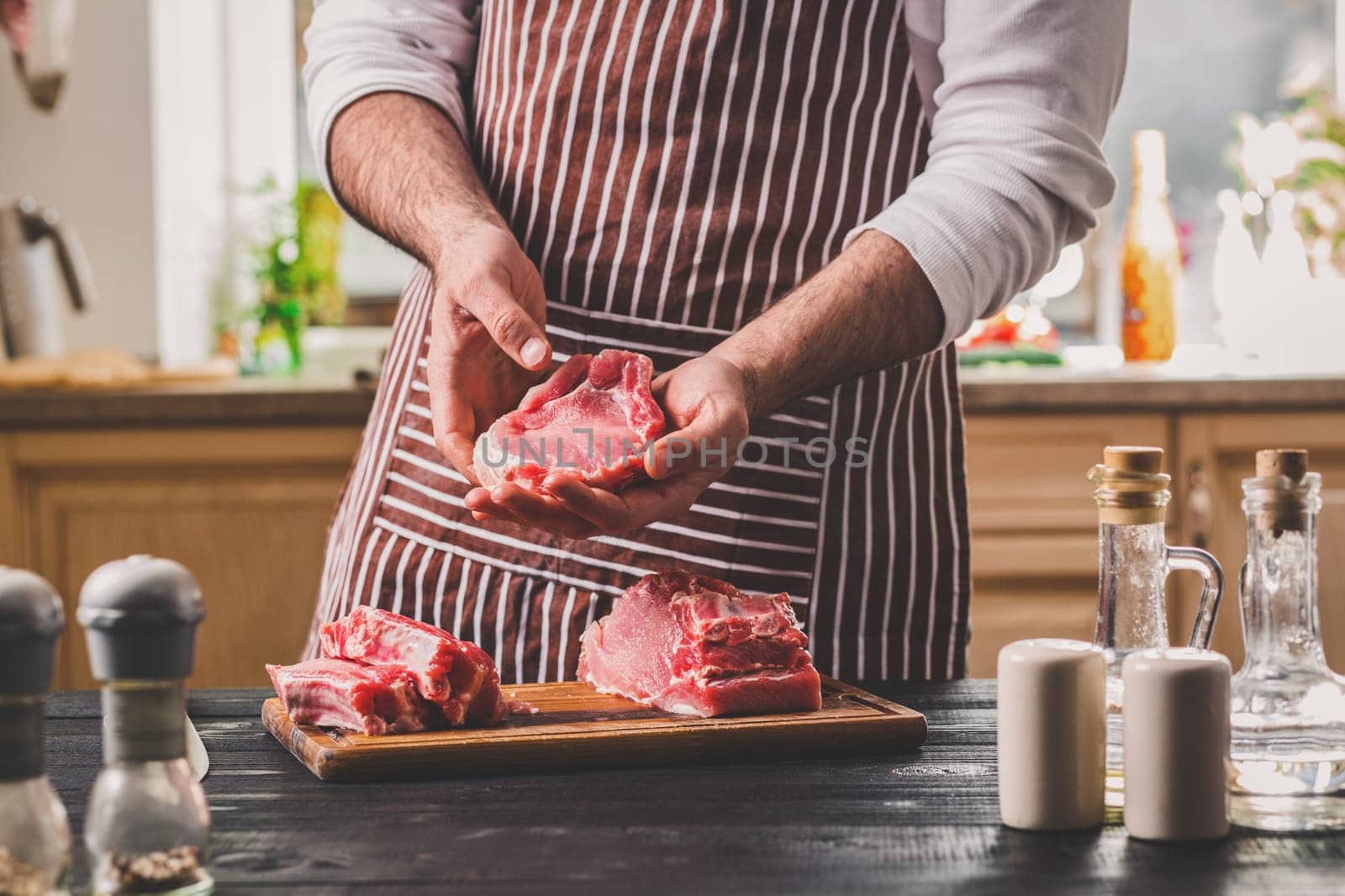 Preparation of dinner. Cooking, processing of meat. Person man's hands marinates meat - sprinkles with salt, pepper. Black wooden table, spices and herbs in the frame.