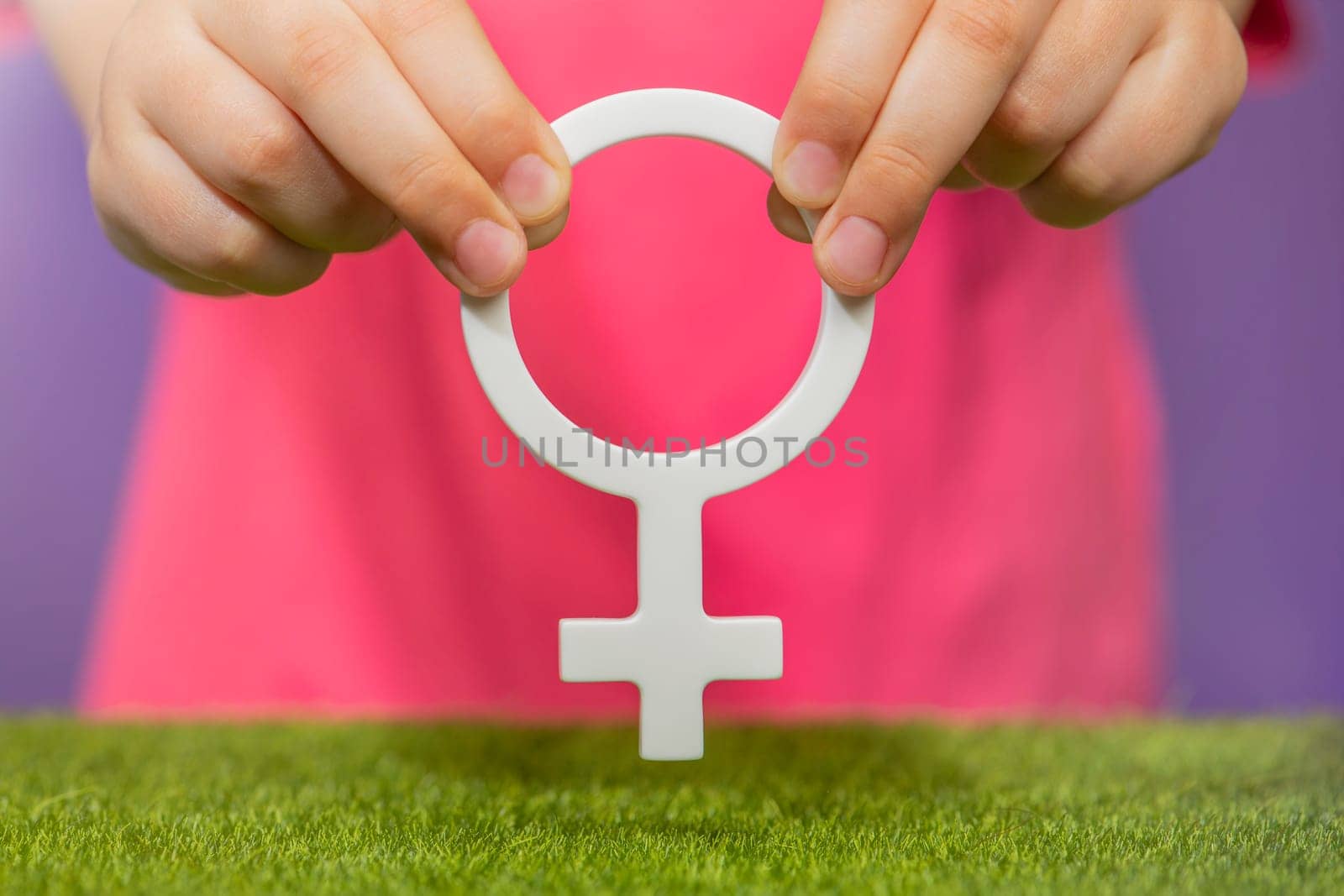 The concept of gender. Female gender symbol in hand on purple background in pink t-shirt with copy space by SERSOL