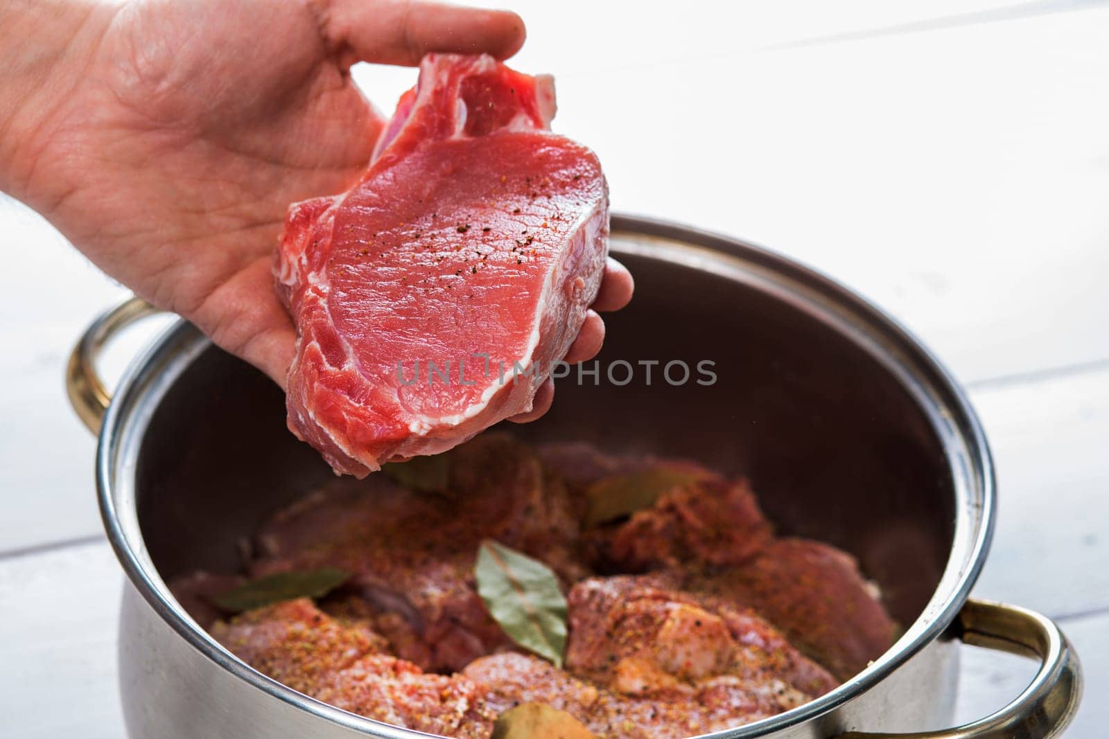Close up of chefs hands spicing the meat. Casserole with raw meat on a white background.